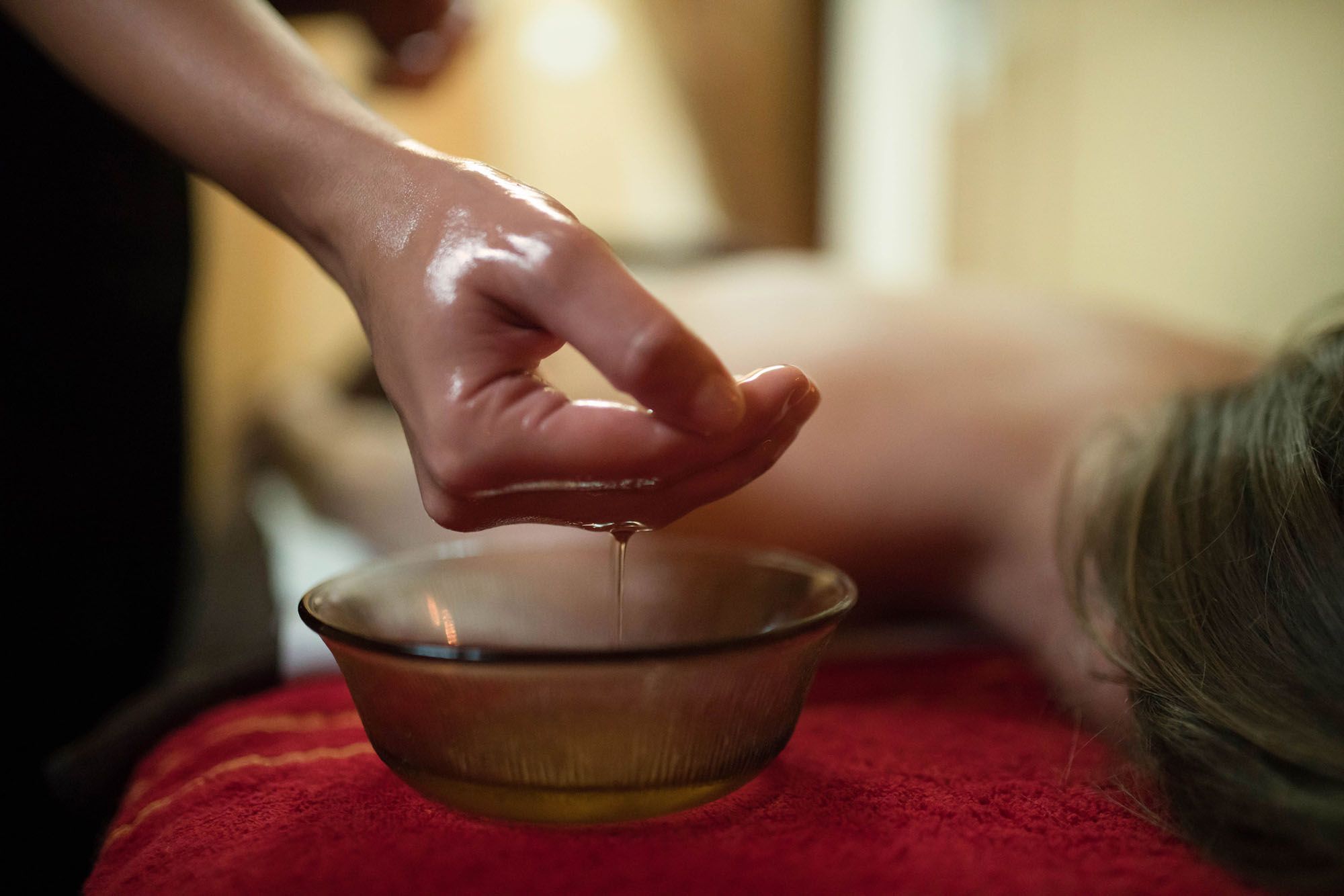 Hand wird in ein Schälchen mit Massageöl getaucht
