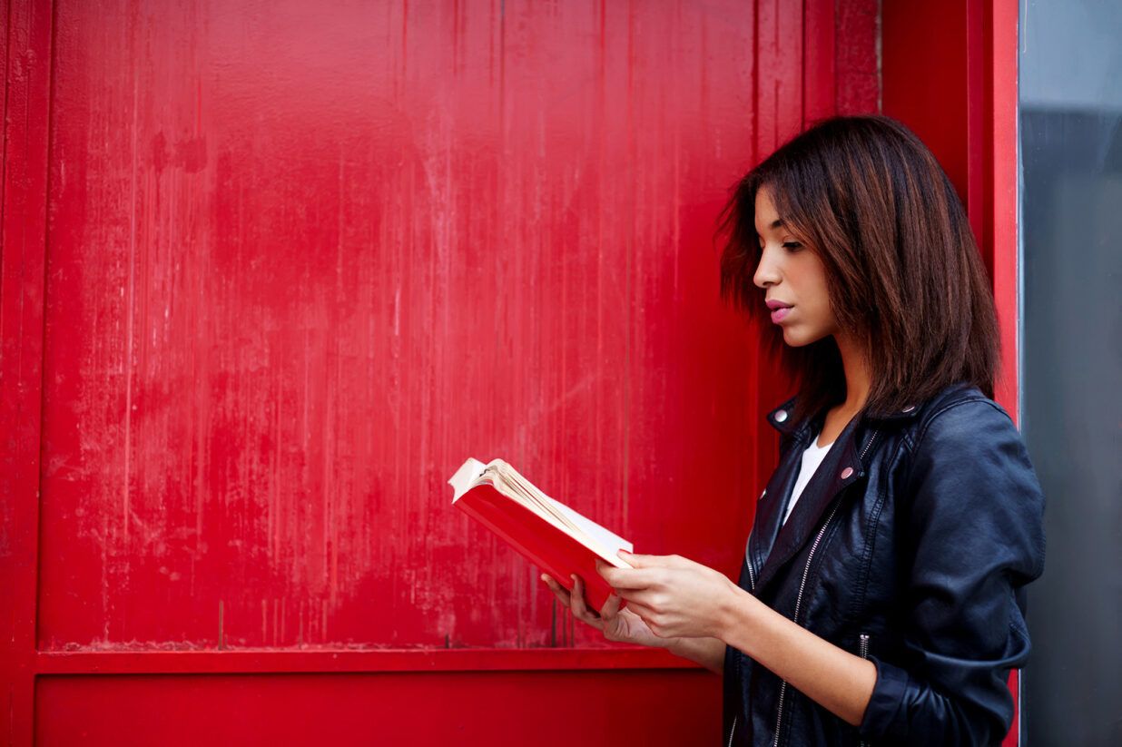 Eine Frau steht vor einem roten Hintergrund und liest in einem Buch mit rotem Einband