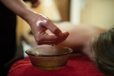 Hand wird in ein Schälchen mit Massageöl getaucht