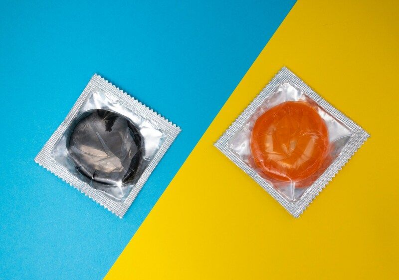 Ein schwarzes und ein orangenes Kondom auf blau-gelbem Hintergrund