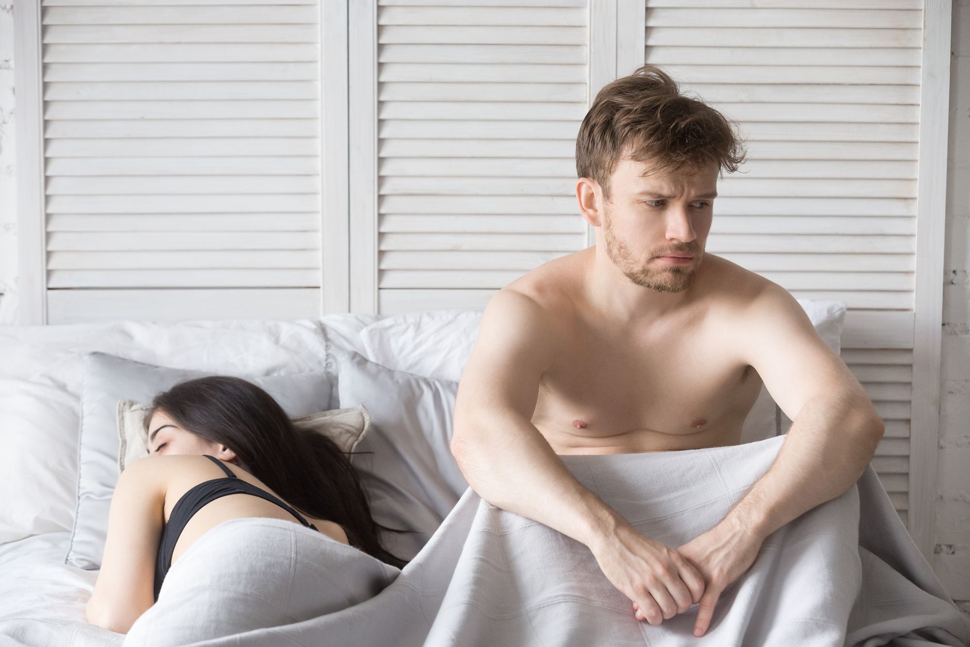 Mann sitzt nachdenklich im Bett, Frau liegt daneben