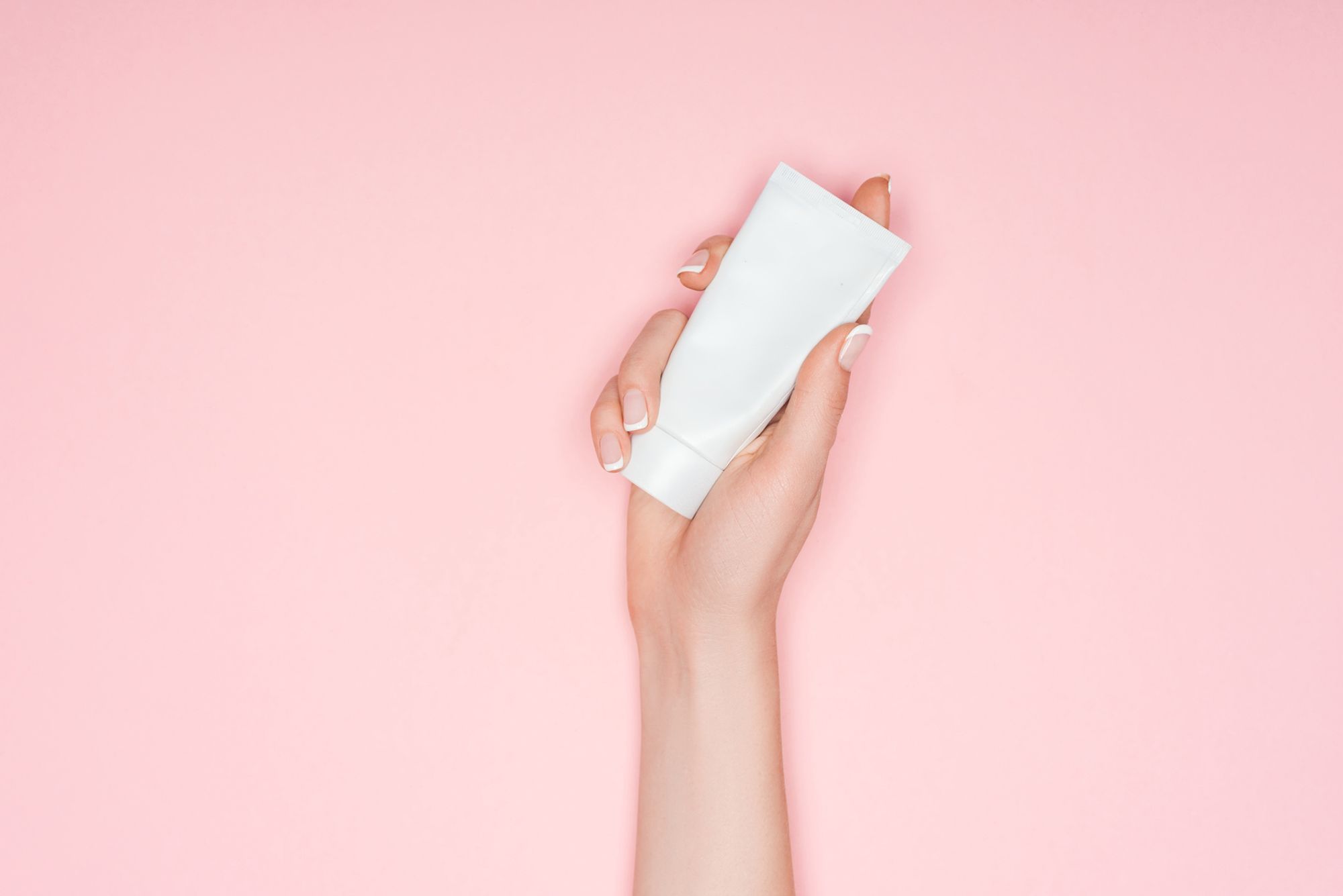 Gleitgel Kondom - Abbildung einer weißen Tube vor einem rosafarbenem Hintergrund, welche von einer weiblichen Hand gehalten wird.
