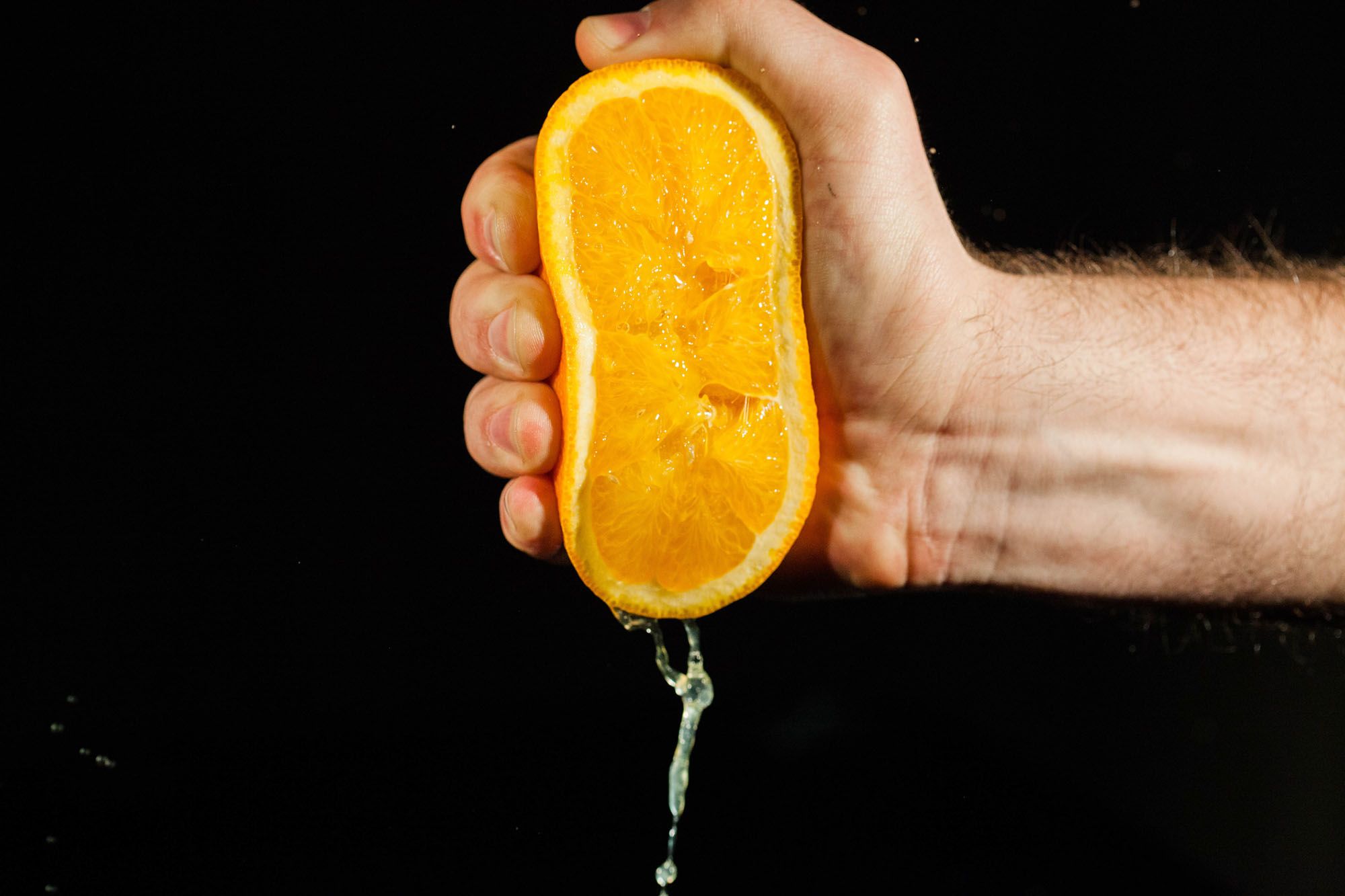 Hand presst eine halbe Orange aus, der Saft tropft nach unten