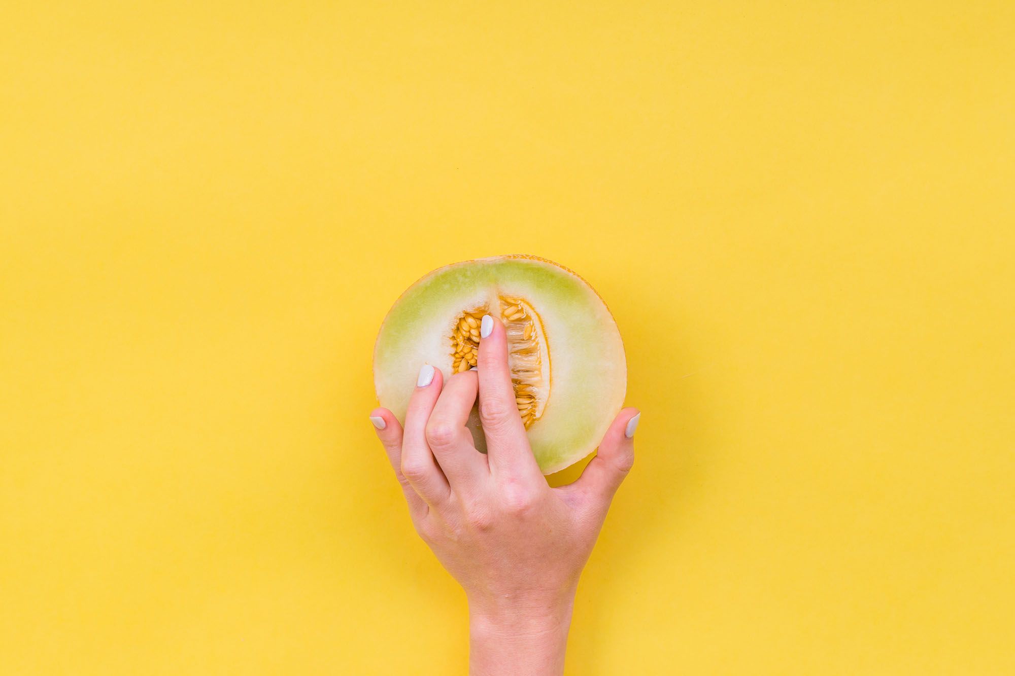 Frau, die ihre Finger in eine halbe Melone einführt