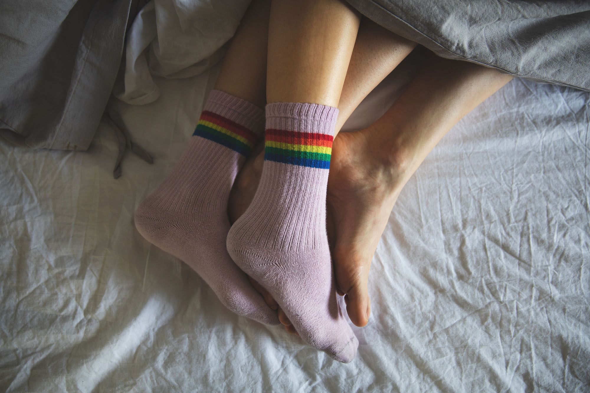 Beim Sex zu früh kommen Tipps - Abbildung zweier Fußpaare, welche im Bett eng umschlungen unter derselben Bettdecke hervorschauen.