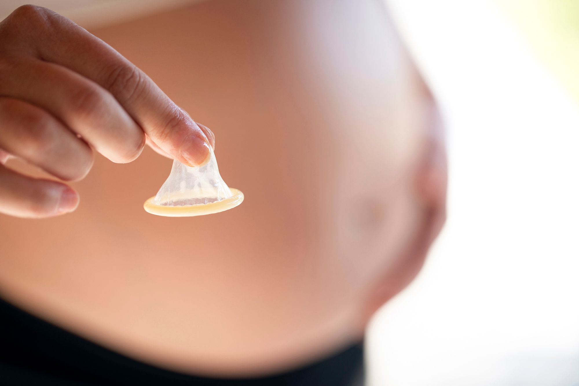 Schwangere Frau hält ein Kondom in der Hand