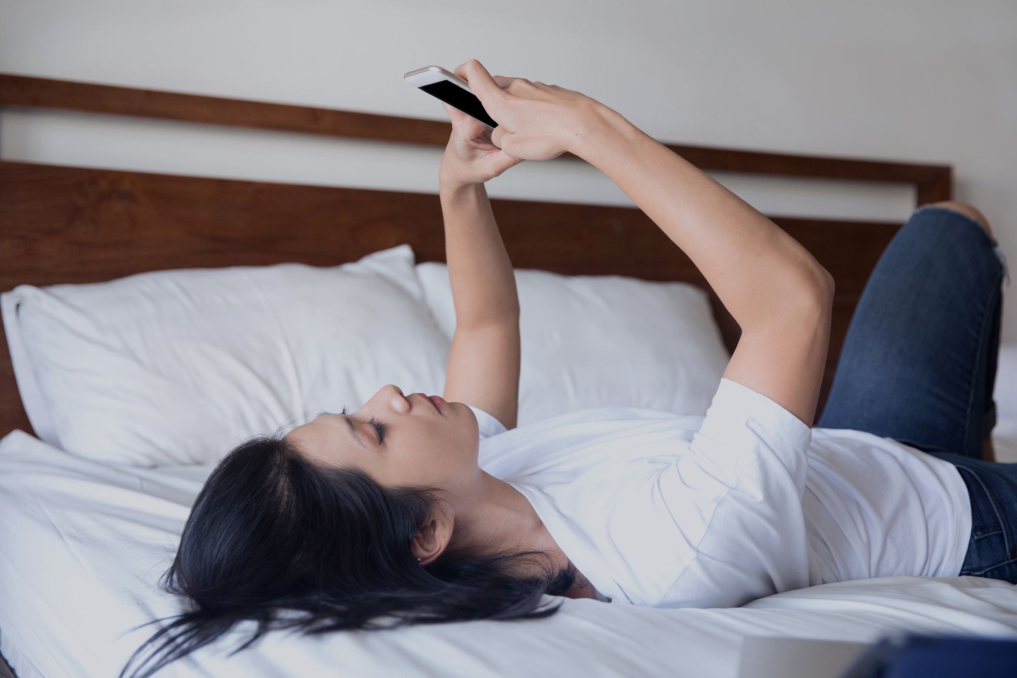 Frau liegt auf dem Rücken im Bett und hält das Handy in beiden Händen