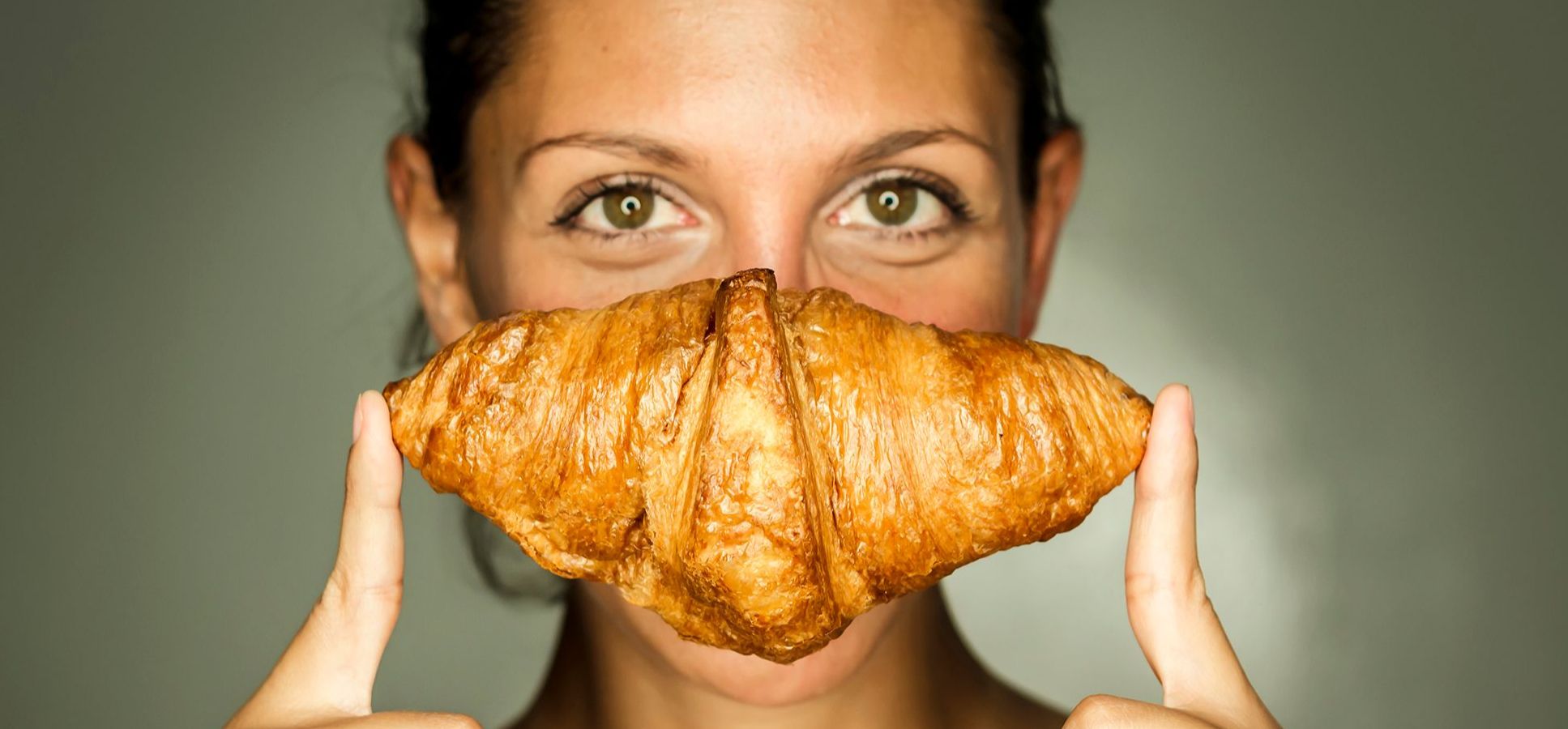 Frau hält sich ein Croissant vor das Gesicht