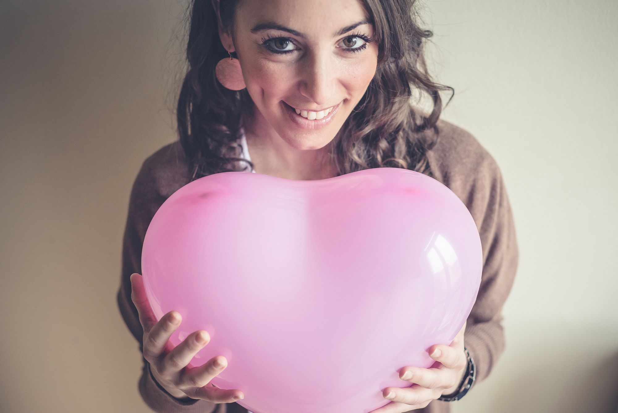 Looner Fetisch - Abbildung einer lächelnden Frau, die einen Ballon in Herzform in die Kamera hält.