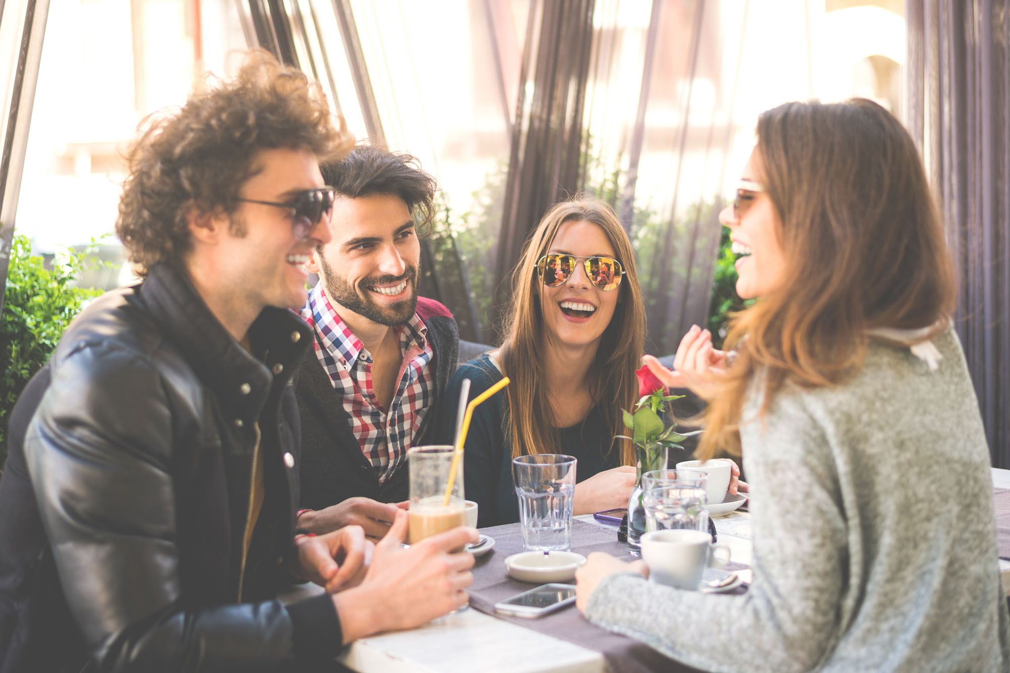 Partnertausch mit Freunden -  Abbildung zweier lachender Hetero-Paaren, welche gemeinsam am Tisch sitzen und Kaffee trinken.