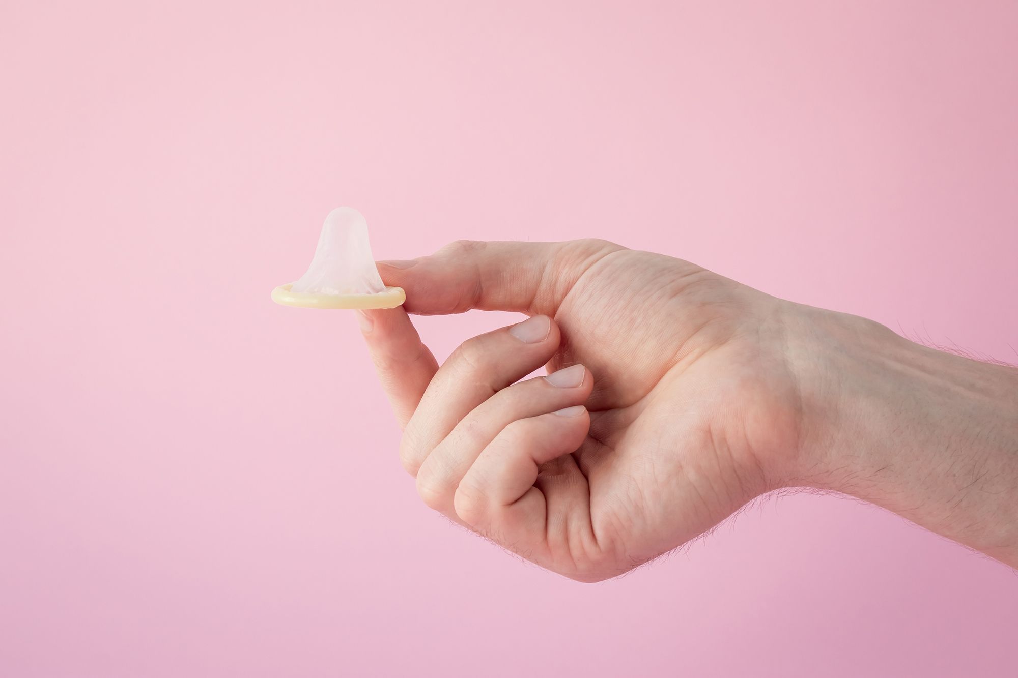 Hand, die ein Kondom zwischen Zeigefinger und Daumen halt vor rosa Hintergrund