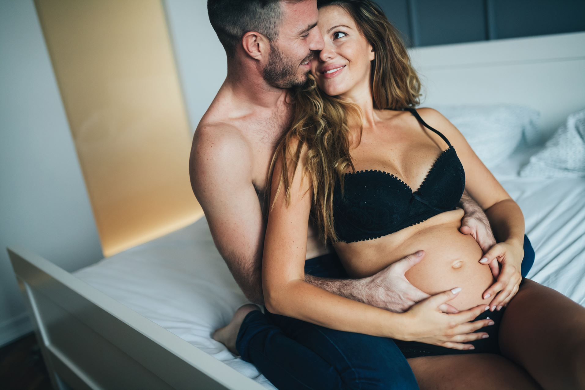 Schwangere Frau lehnt sich auf den Bett sitzend an den Partner an