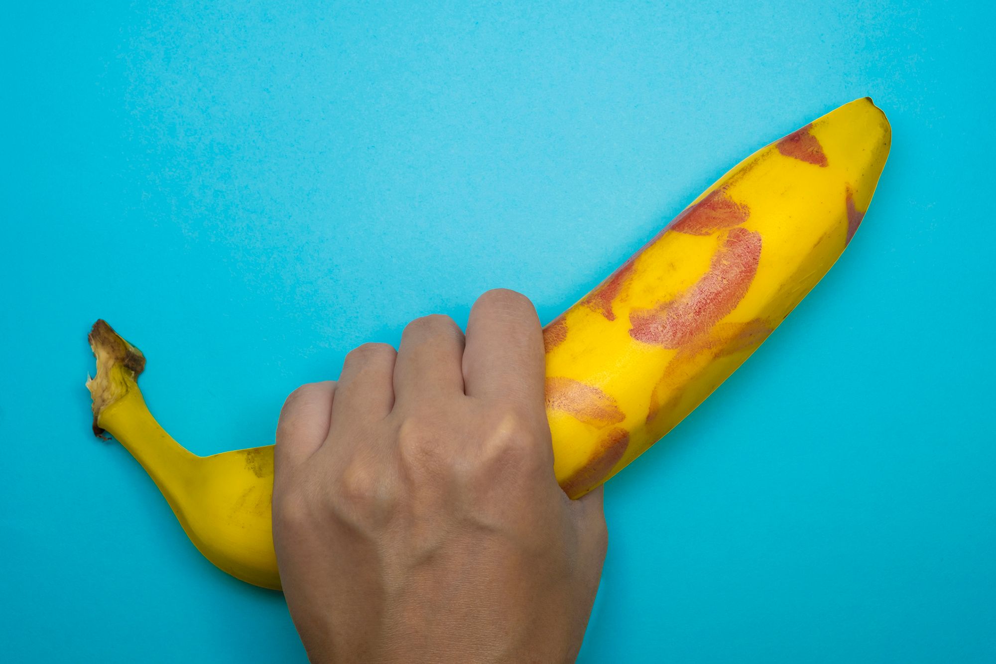Hand umfasst eine Banane mit Lippenstift-Abdrücken auf der Schale.
