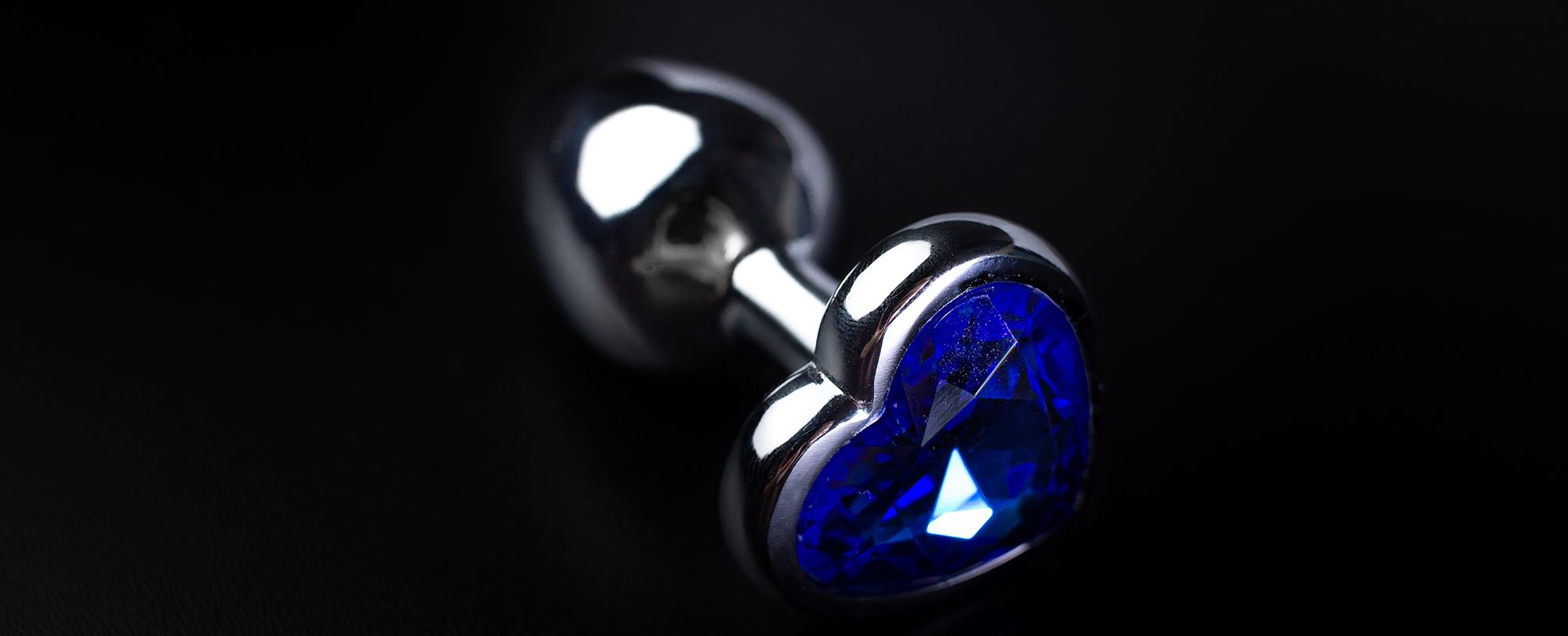 Silberner Analplug mit blauem Stein in Herzform auf schwarzem Hintergrund