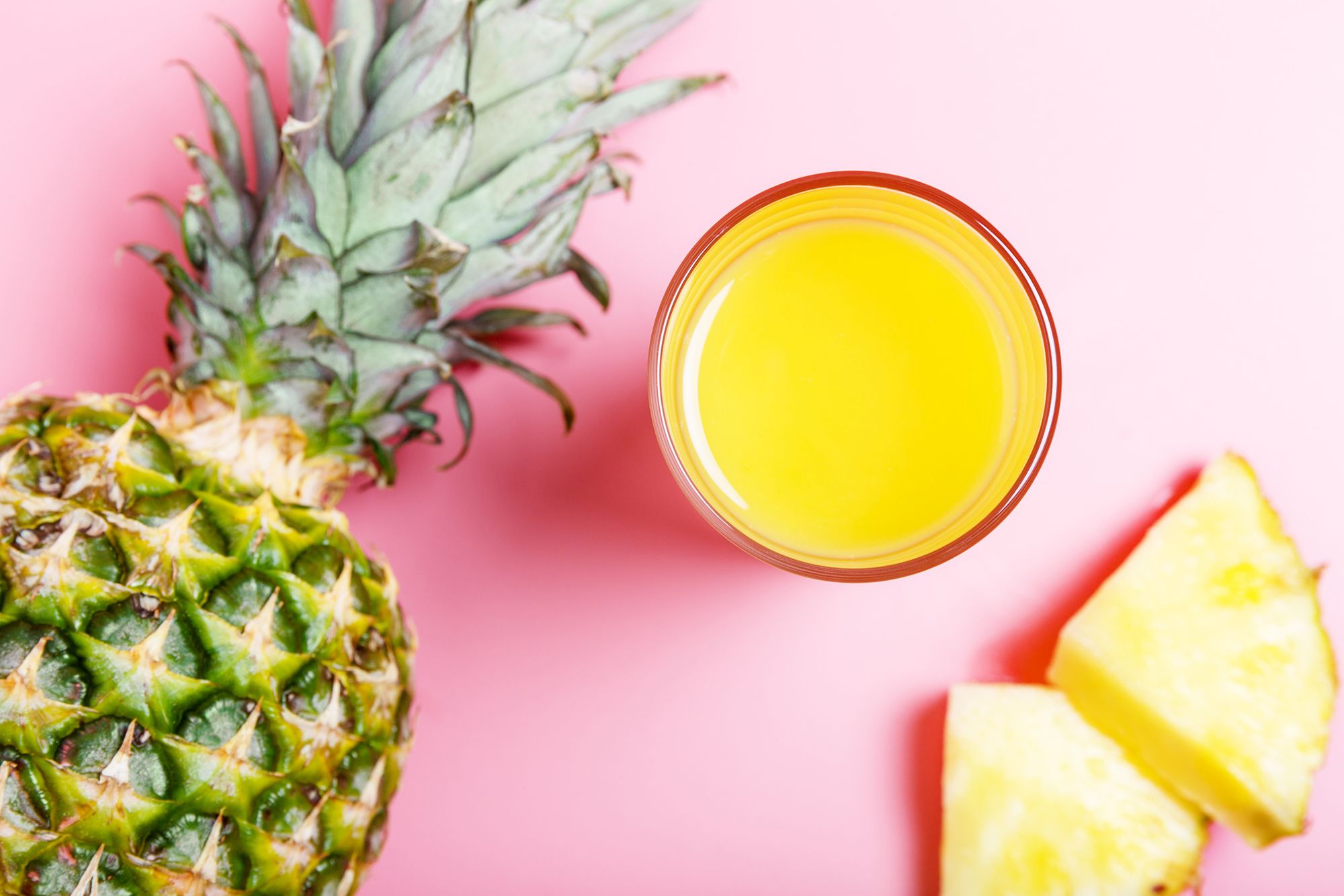 Ananas und ein Glas mit Ananassaft auf pinkem Hintergrund