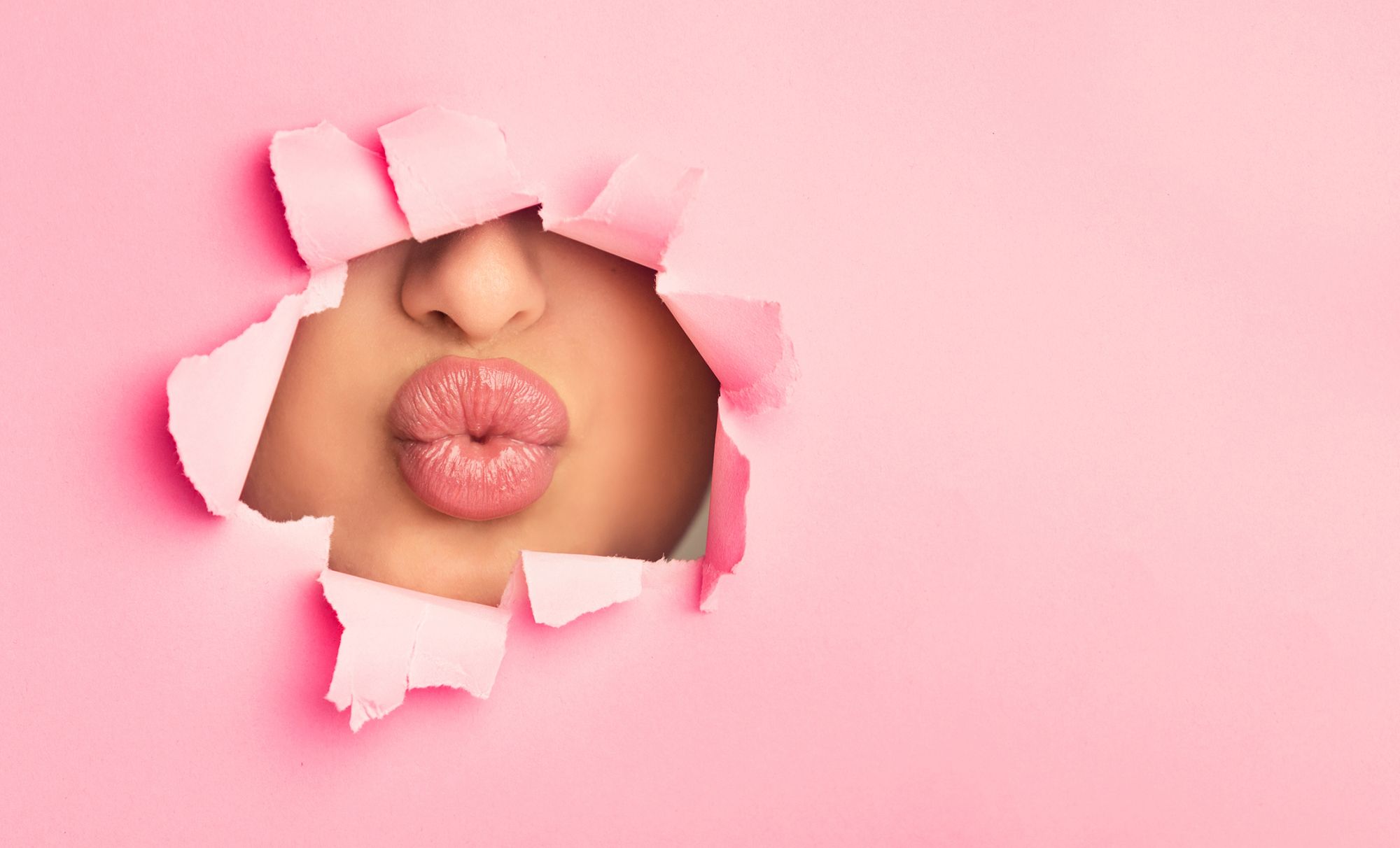Kussmund einer Frau, der durch ein Loch in einer pinken Papierwand sichtbar ist