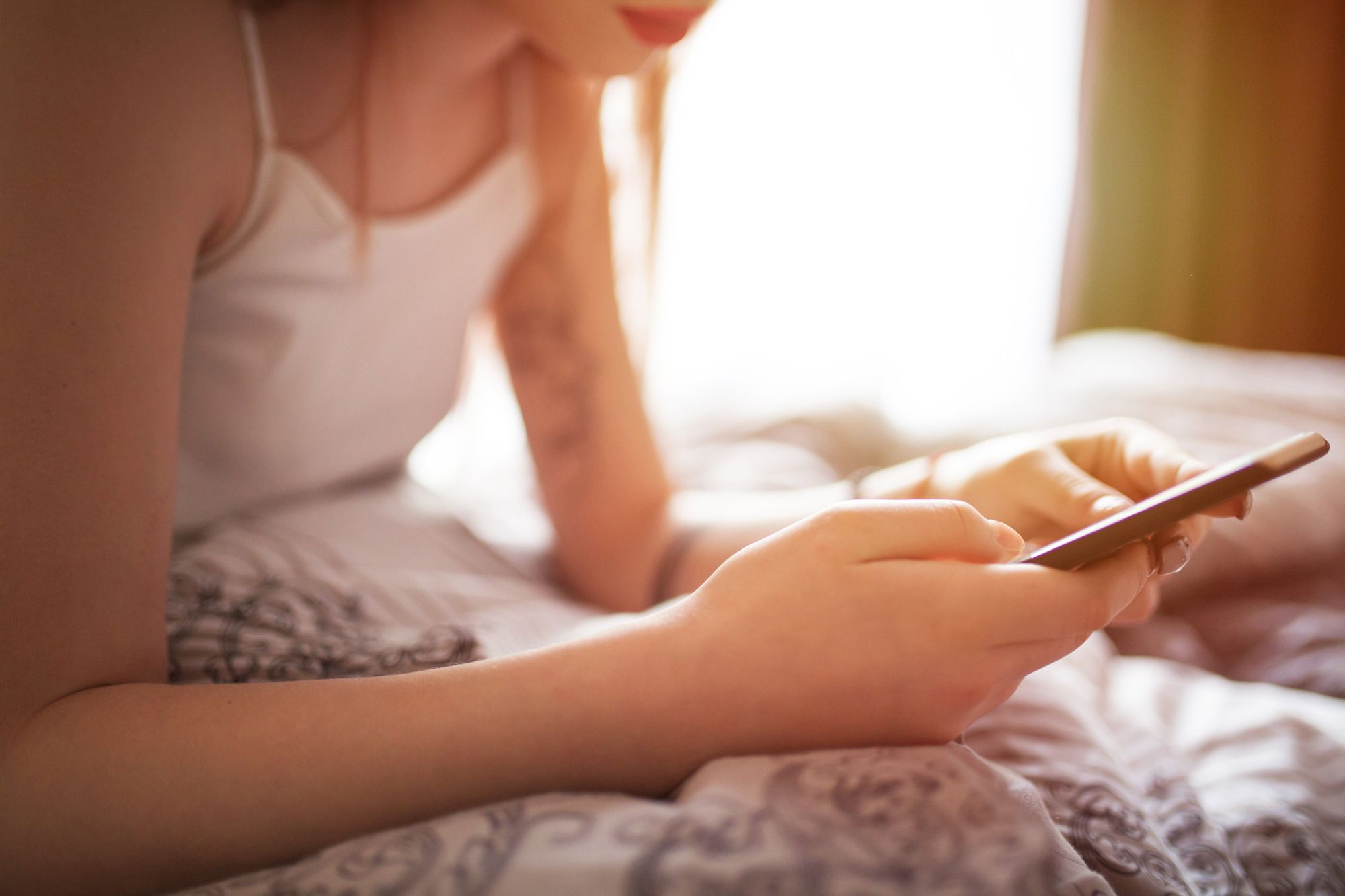 Frau liegt mit ihrem Smartphone in der Hand im Bett