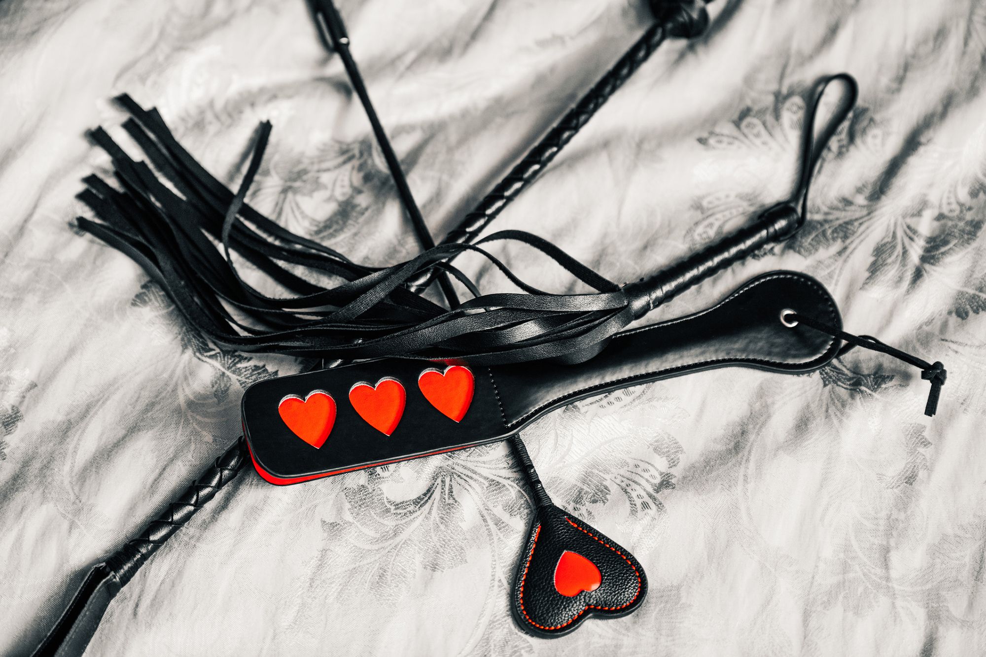 Schwarze Peitsche, Schwarze Gerte mit rotem Herz und schwarzes Paddle mit drei roten Herzen auf Federn