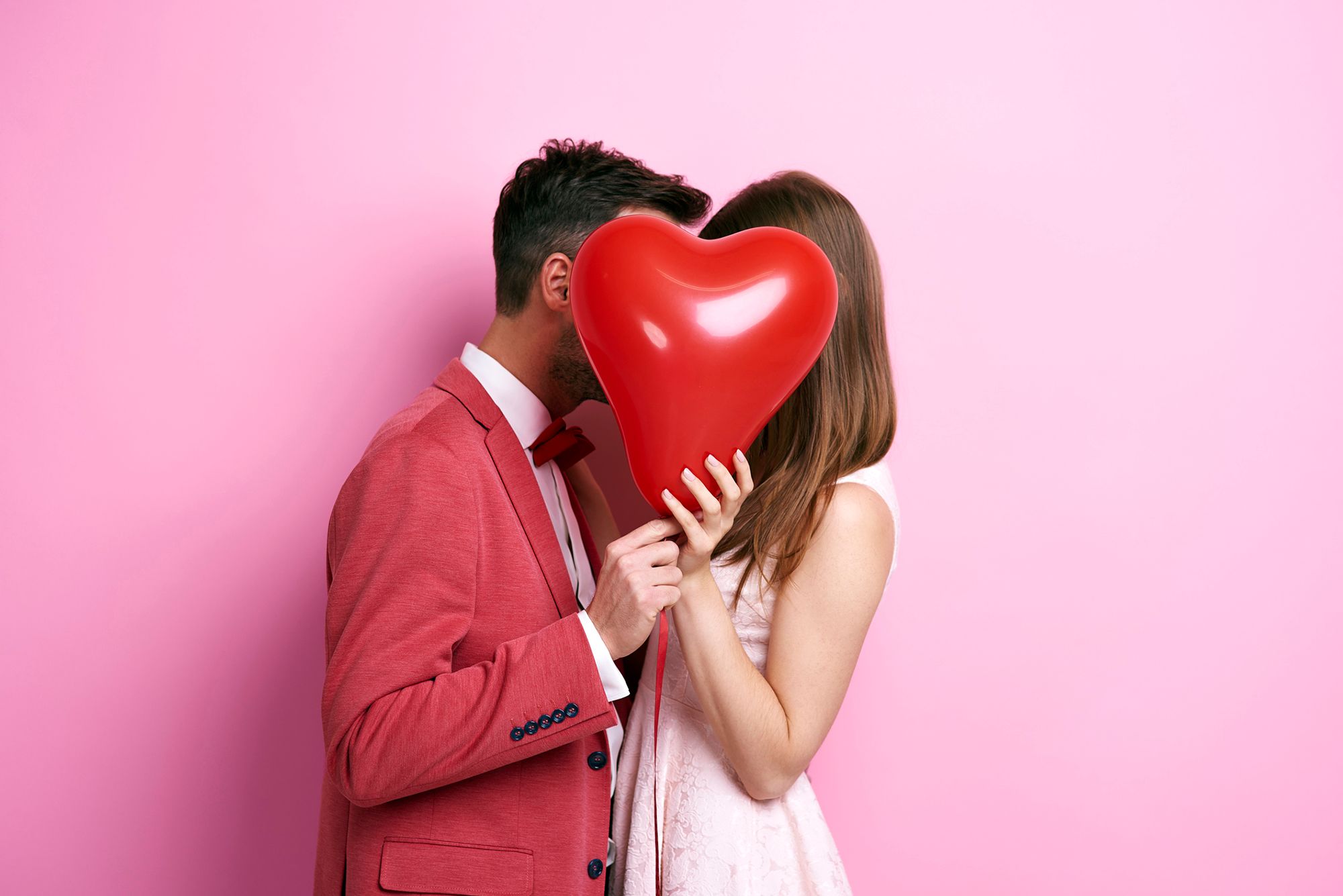 Mann und Frau küssen sich hinter einem Herzluftballon