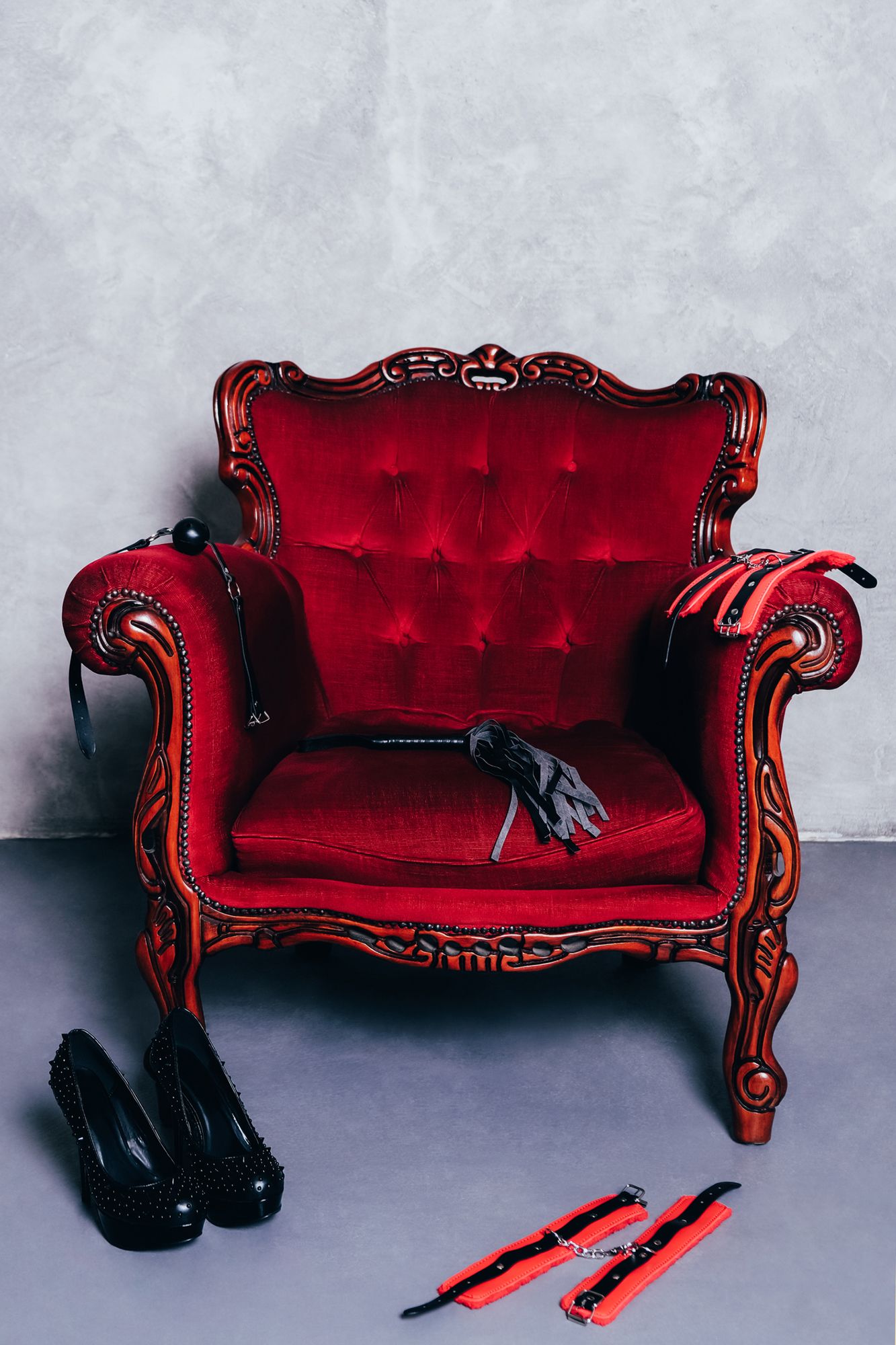Ein roter Sessel mit High Heels und Bondage Accessoires davor