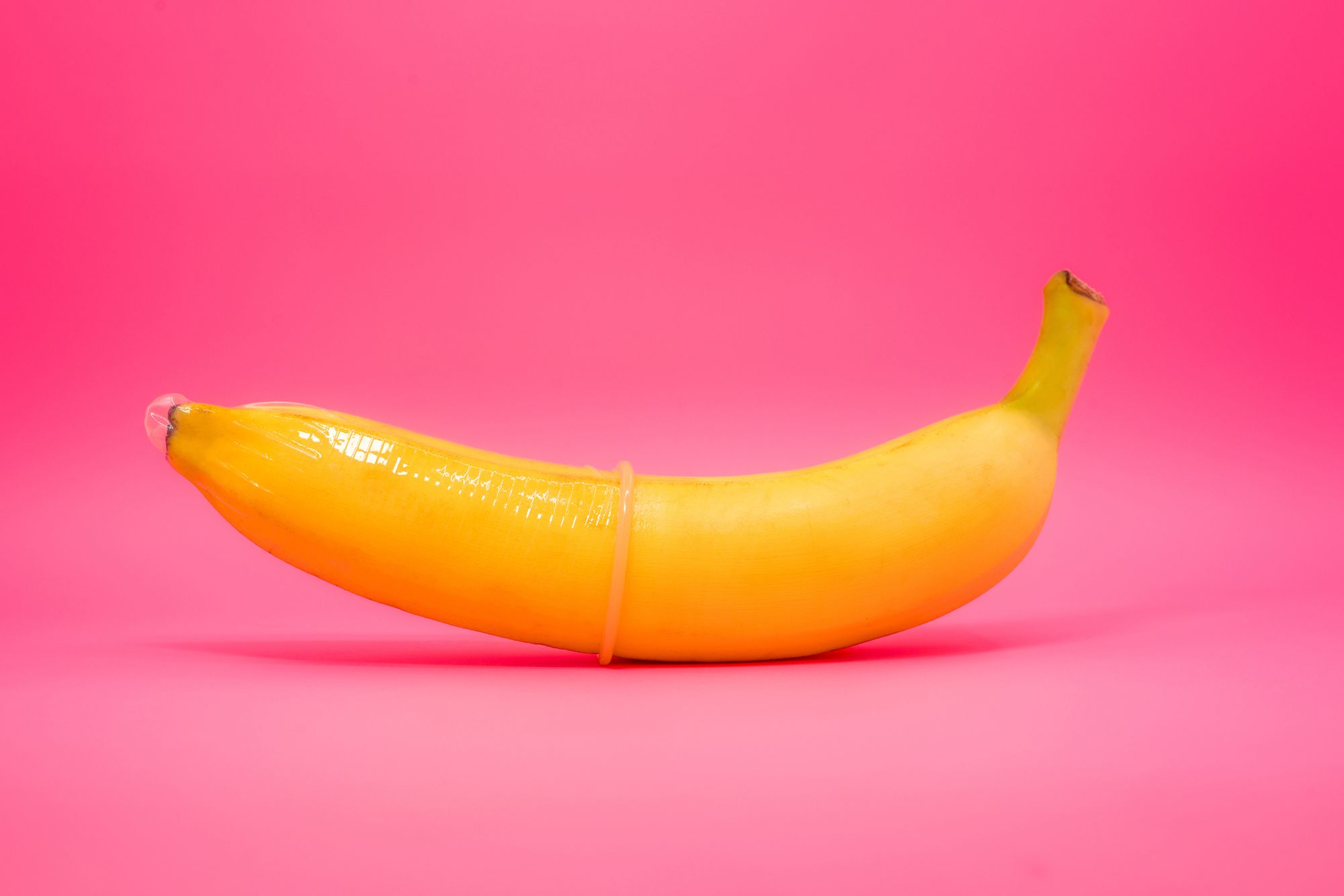 Eine Banane mit einem übergestülpten Kondom vor einem pinken Hintergrund