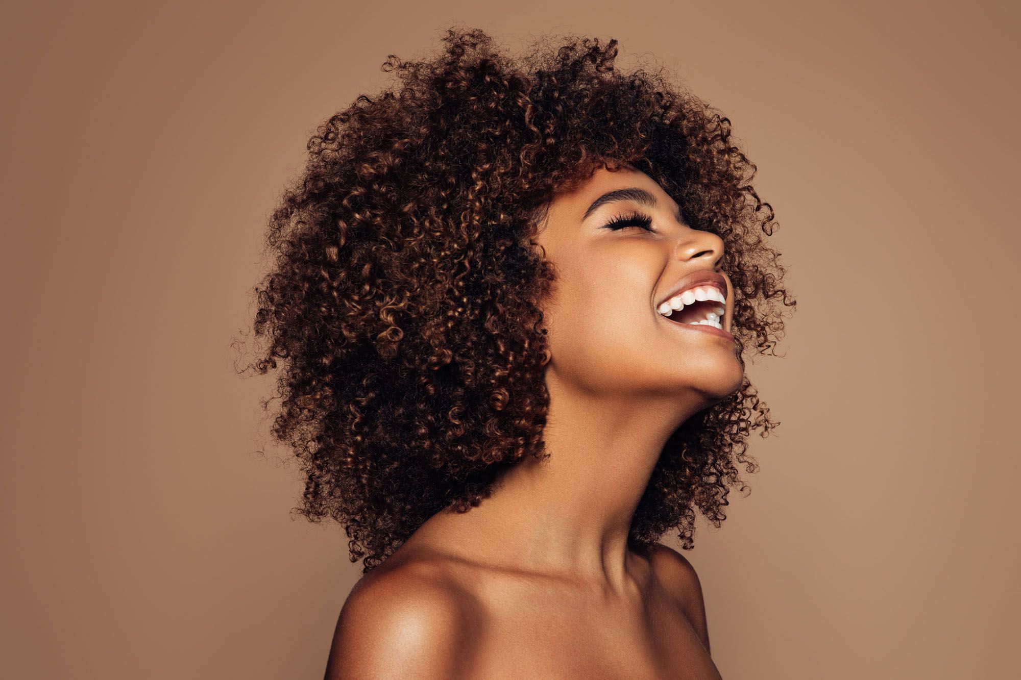Lachende, freizügige Frau mit Afro vor braunem Hintergrund