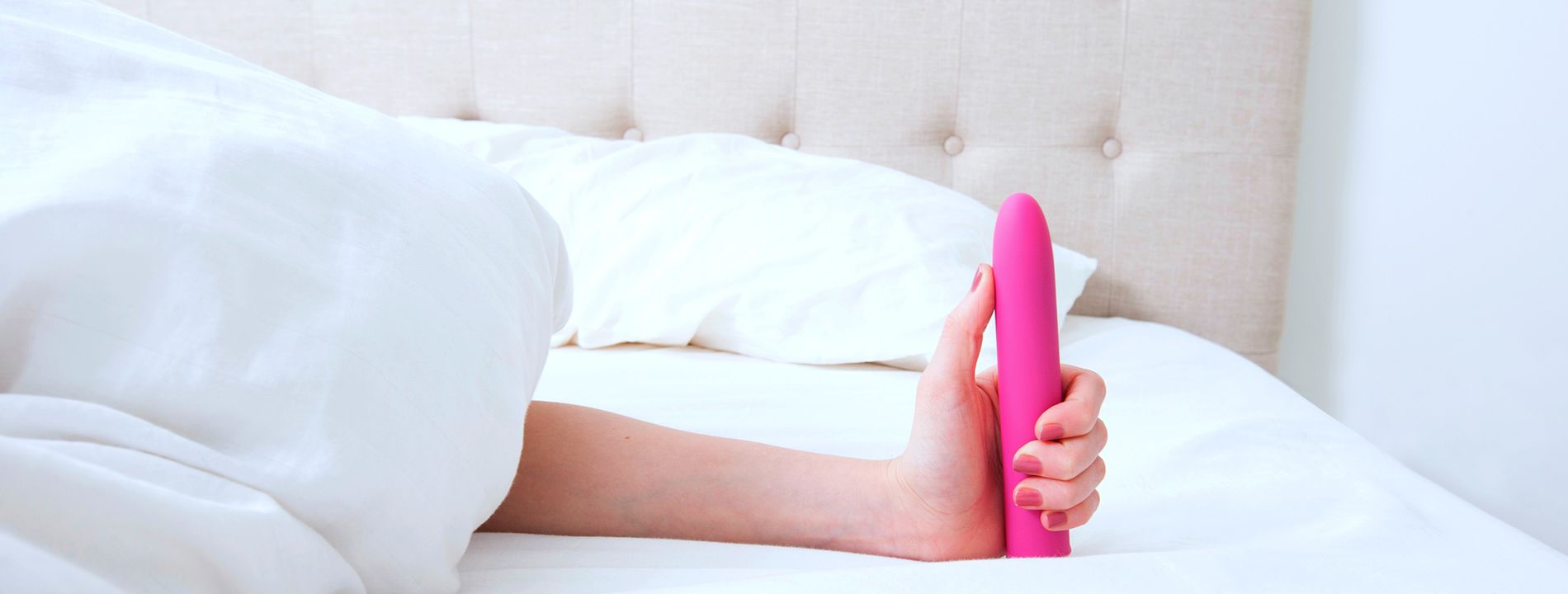 Frau im Bett hält pinken Vibrator in der Hand