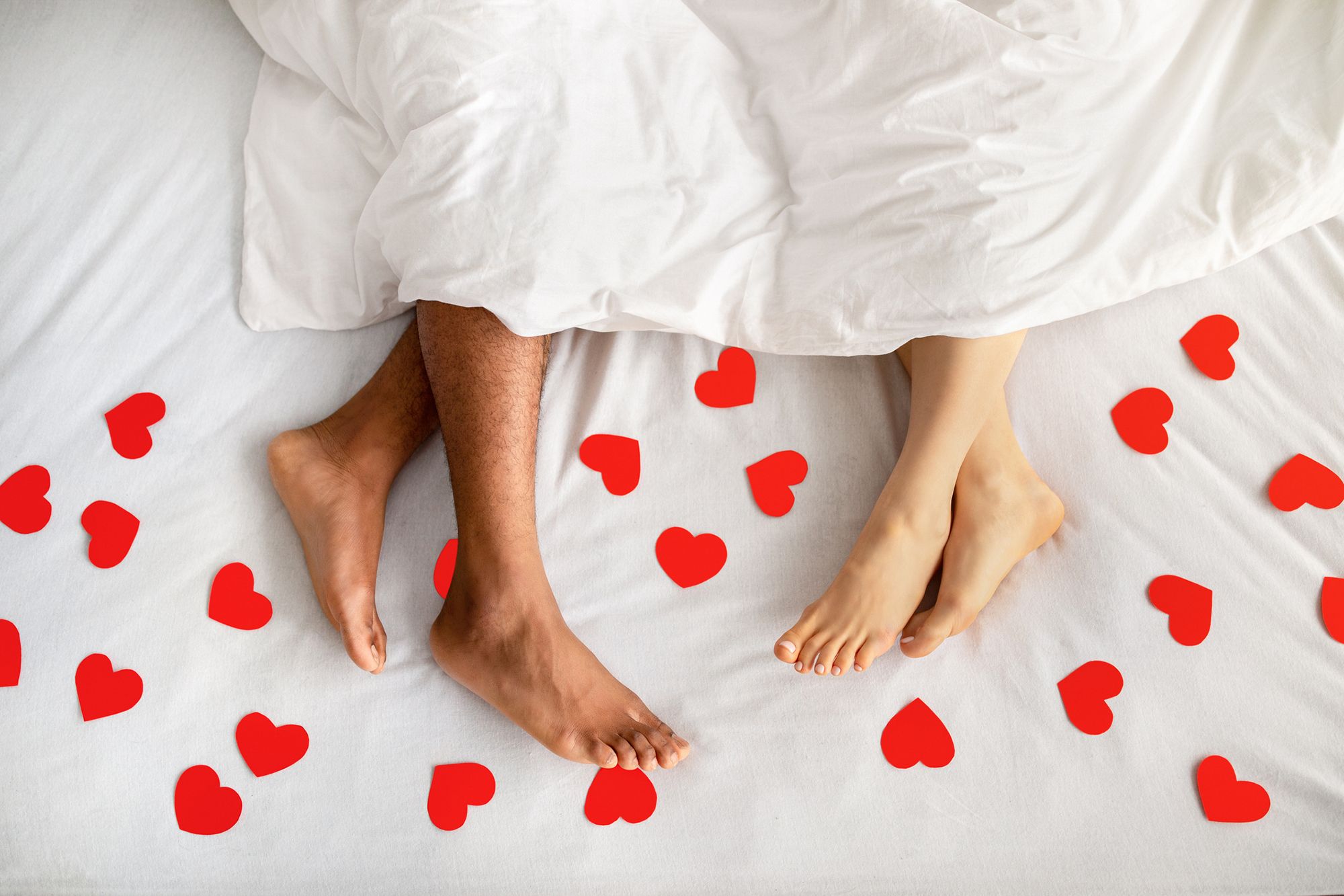Paar im Bett mit roten Papierherzen auf dem Laken