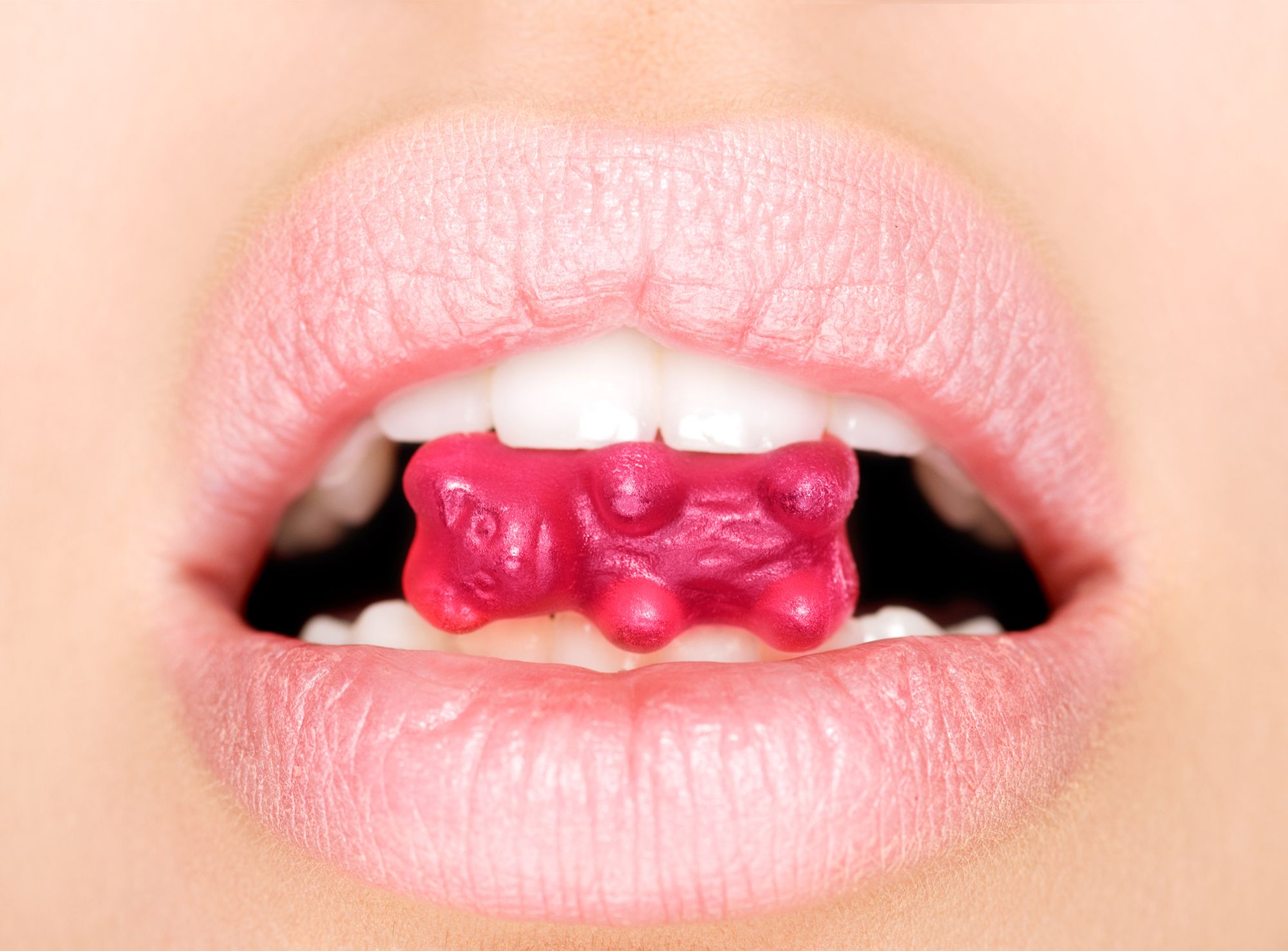 Frau hält ein Gummibärchen zwischen den Zähnen