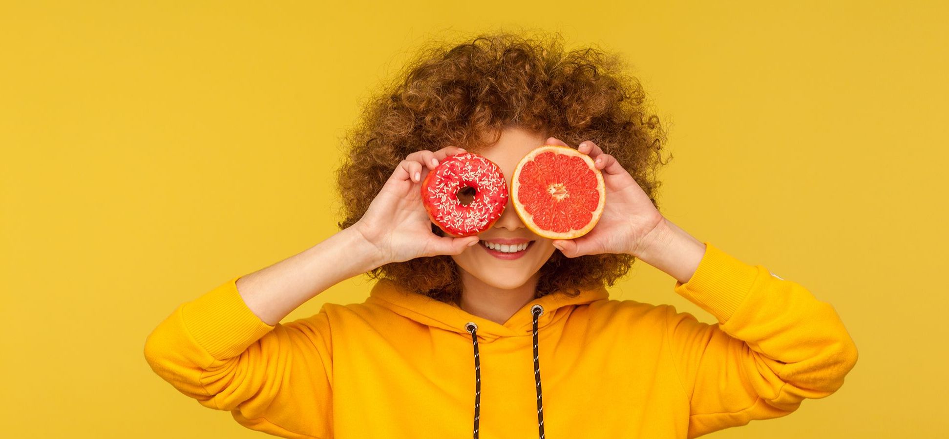 Frau, die einen Donut und eine halbe Orange vor ihre Augen hält