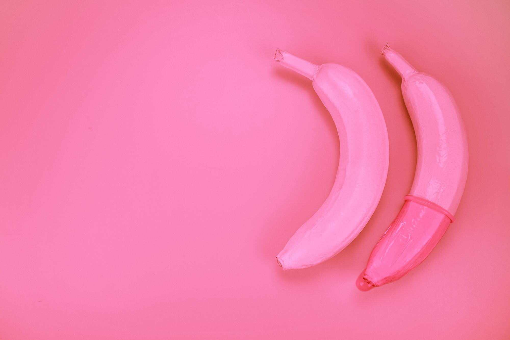 Zwei pinke Bananen, über eine ist ein Kondom gestülpt
