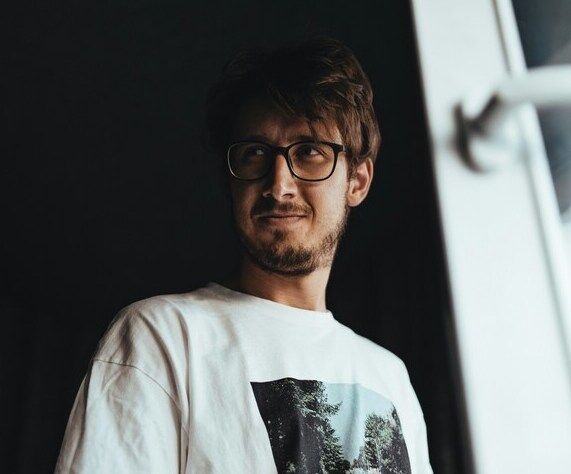 Mann mit Brille und weißen Shirt steht vor einer Tür