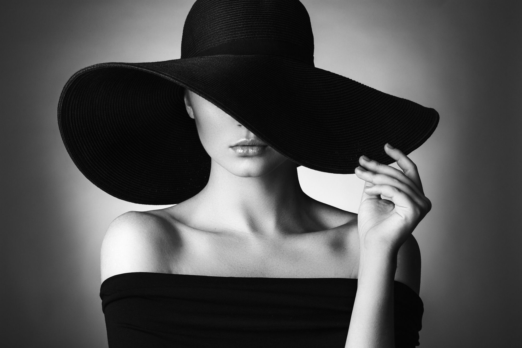 Frau in einem schwarzen Kleid, sie trägt einen großen schwarzen Hut