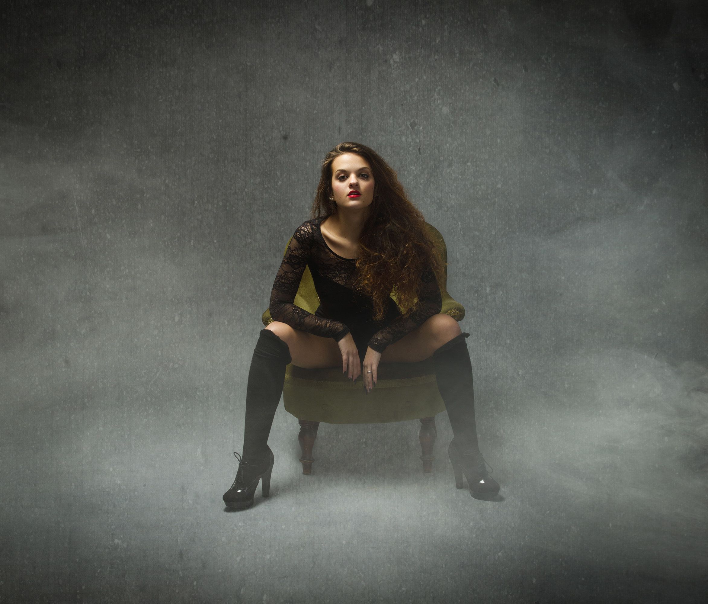 Frau in BDSM-Outfit sitzt mit gespreizten Beinen auf einem Sessel