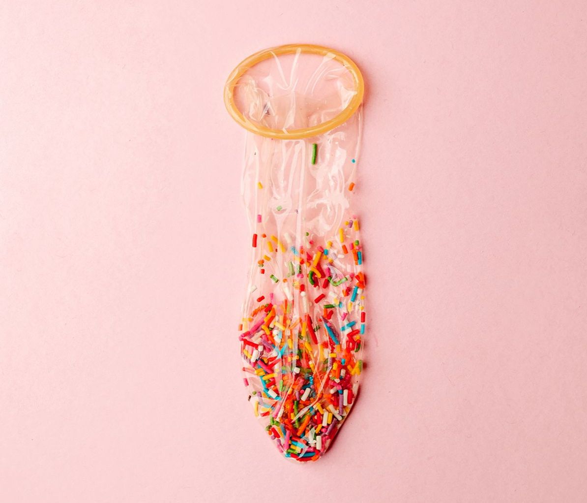 Mit Schokostreuseln gefülltes Kondom vor rosa Hintergrund
