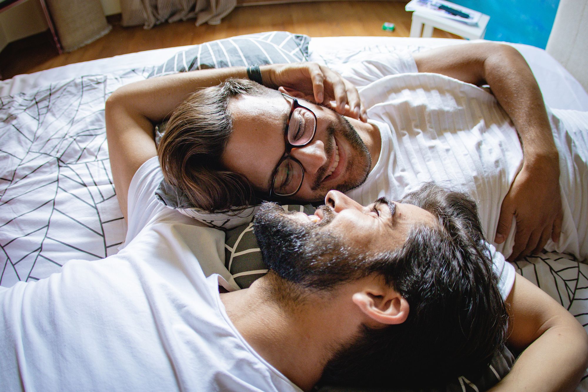 2 Männer liegen im Bett und lächeln sich an