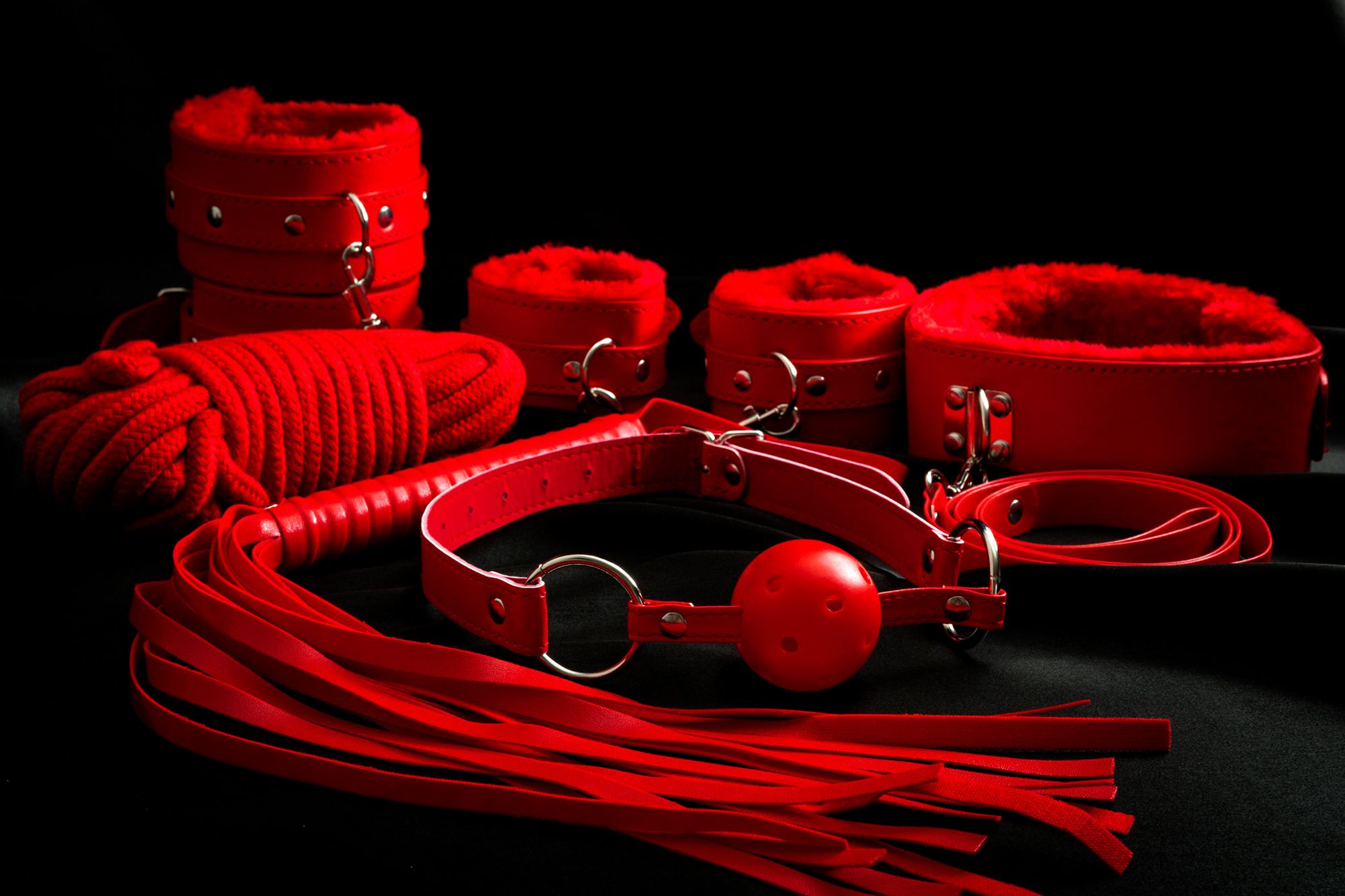 Rote BDSM-Sextoys: Knebel, Seil, Peitsche sowie Handfessel und Fußfesseln