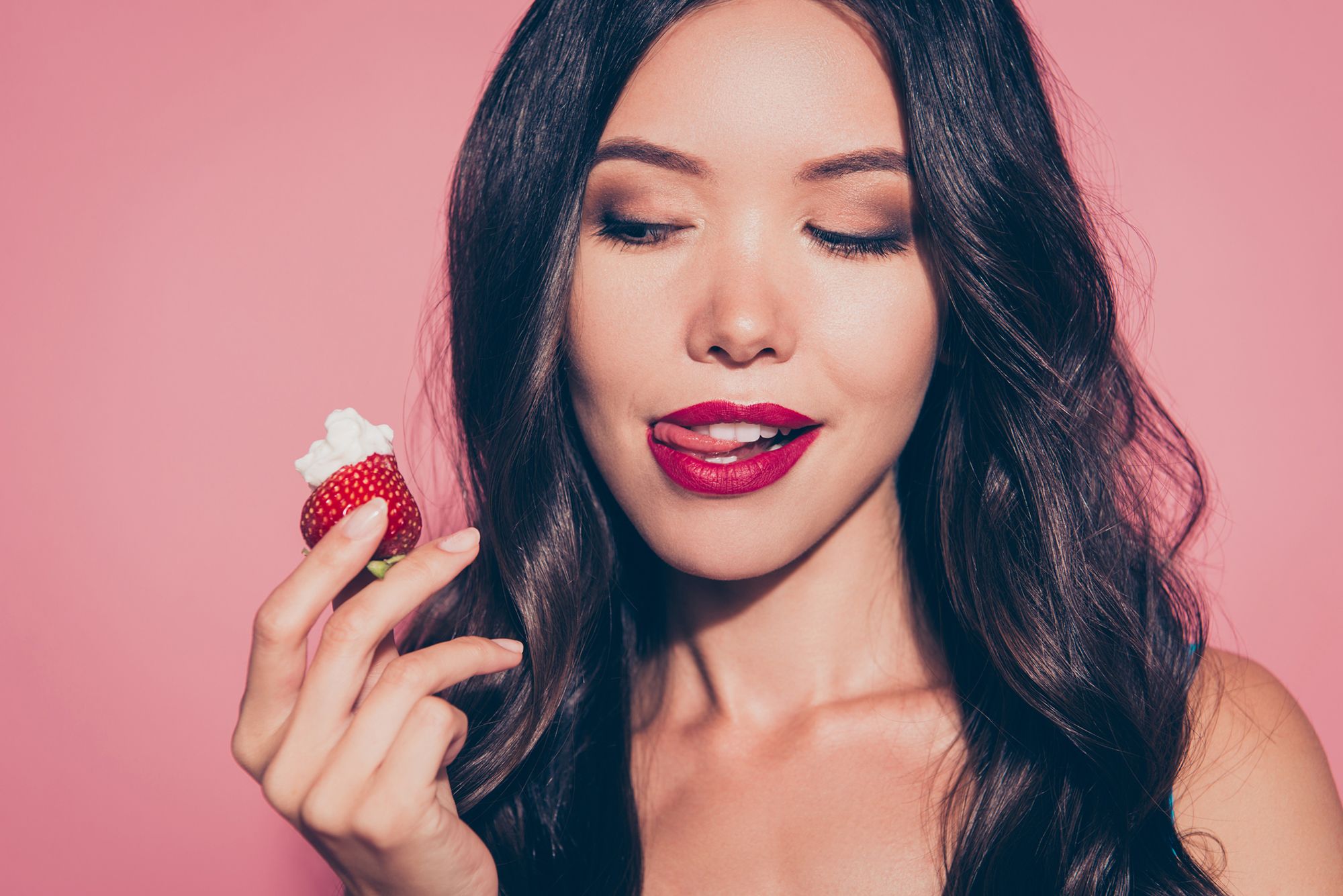 Frau hält eine Erdbeere in der Hand und leckt sich die Lippen