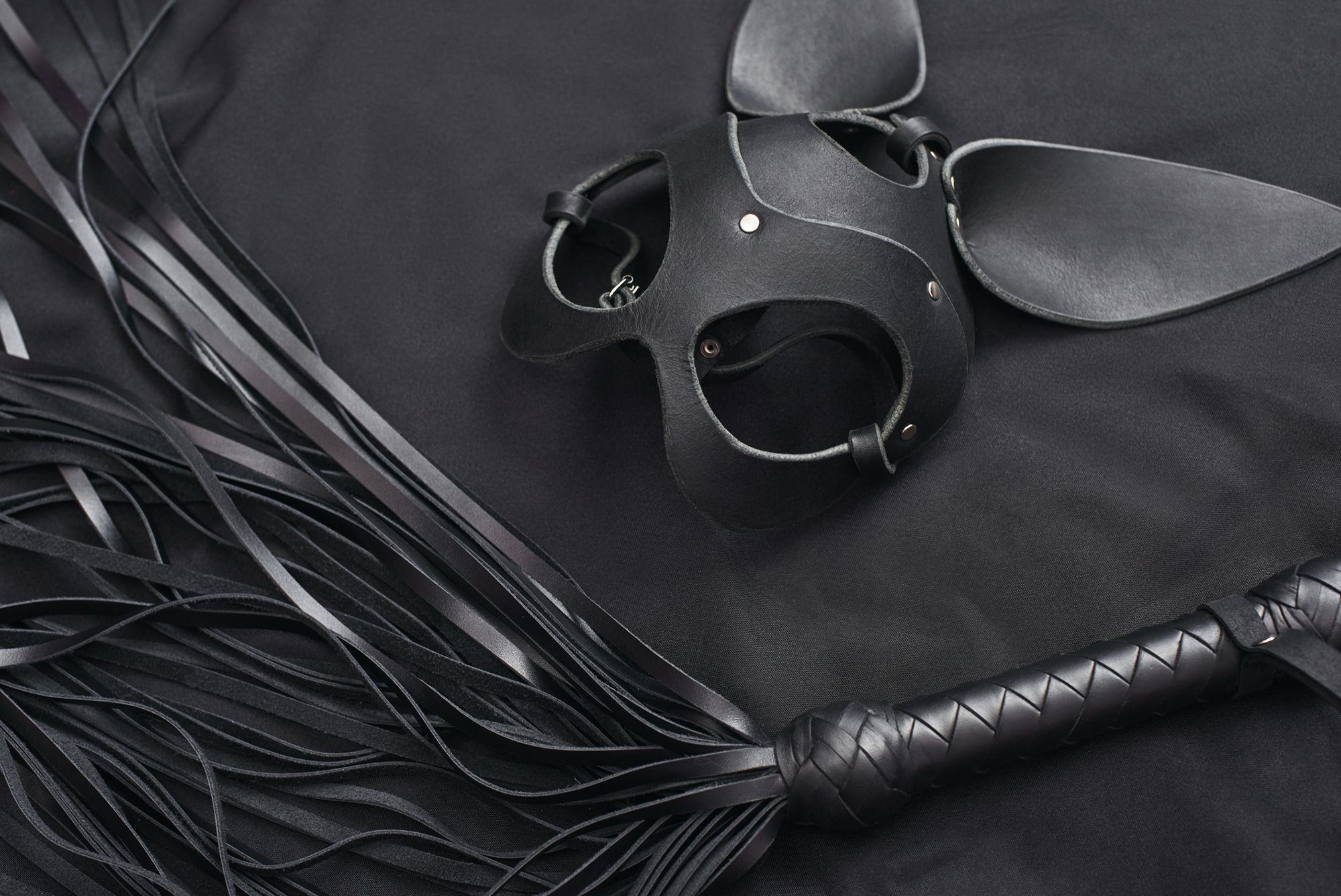 Schwarze Peitsche und Hasenmaske auf schwarzem Hintergrund