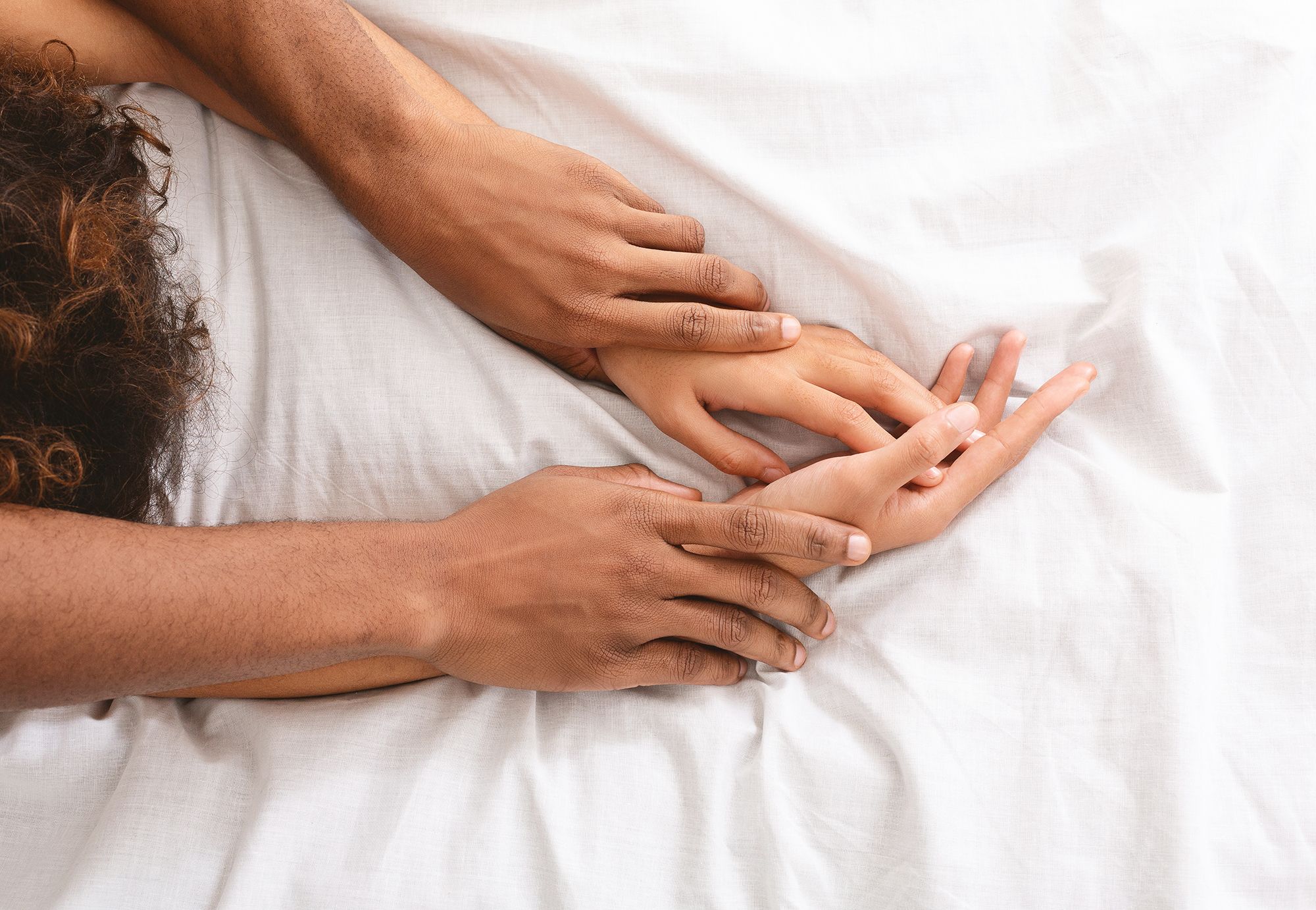 Hände von Mann und Frau im Bett