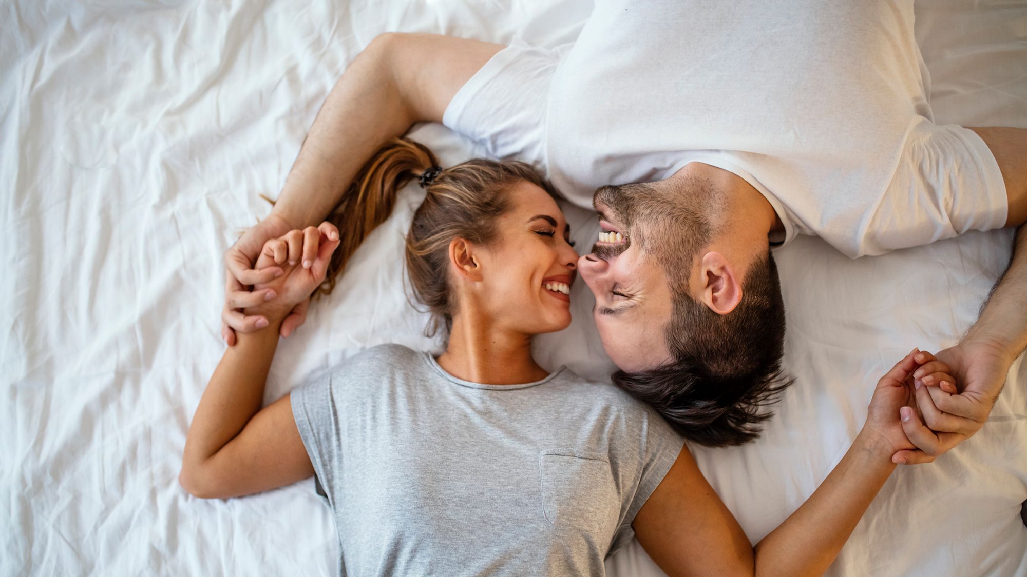 Paar hält sich lächelnd im Bett an den Händen