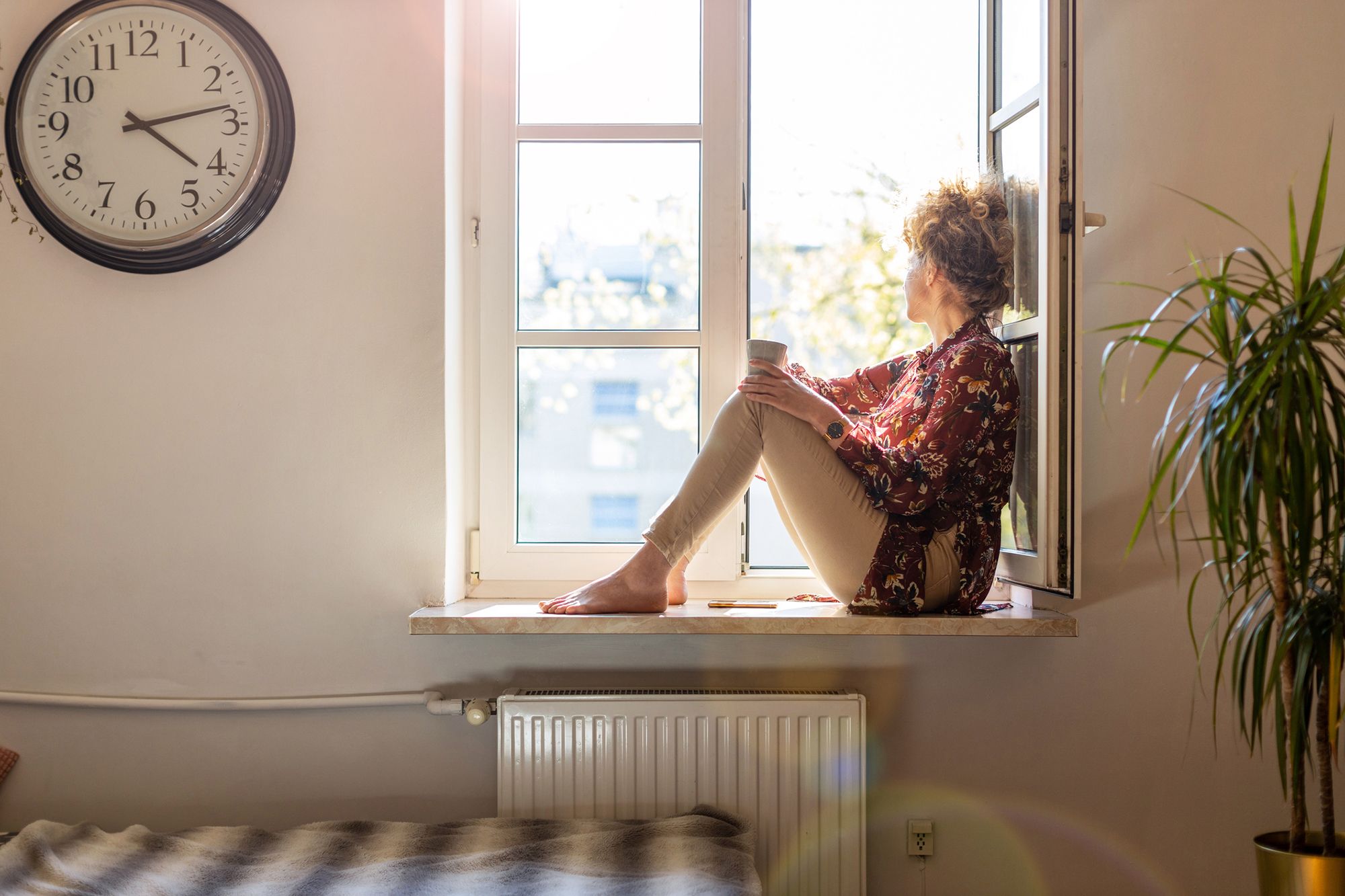 Frau sitzt nachdenklich auf dem Fensterbrett