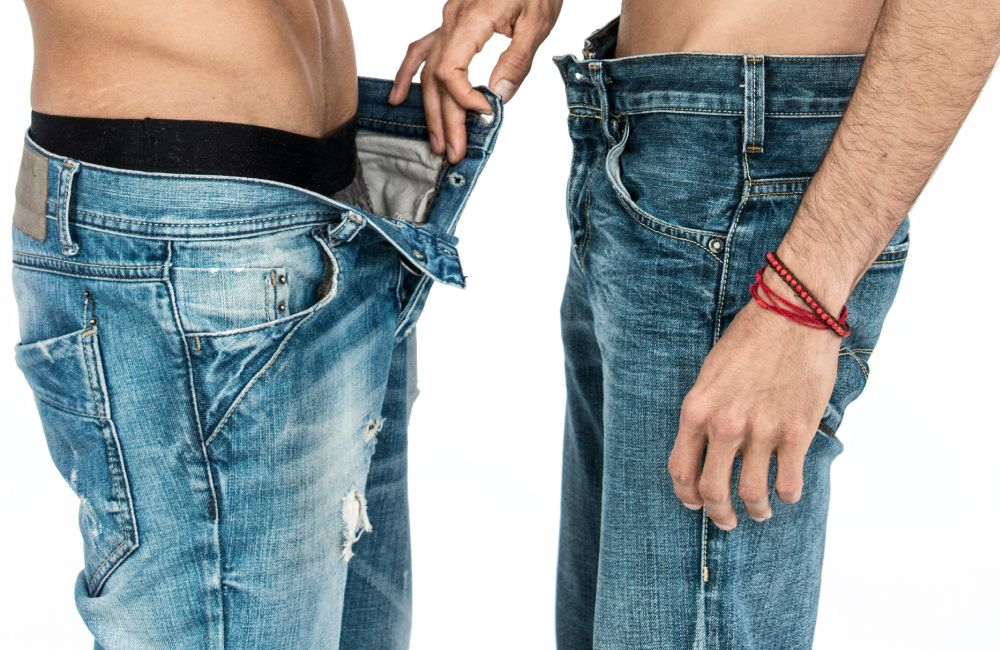 Zwei Männer in Jeans, die sich gegenüber stehen und einer öffnet die Hose vom anderen