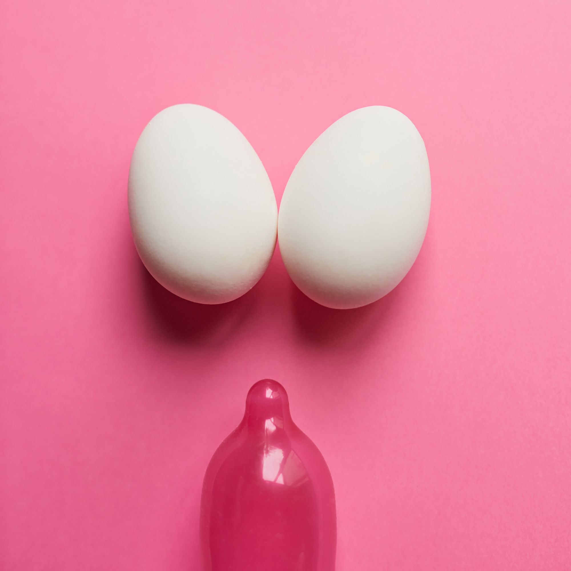 Zwei Eier und ein Kondom vor einem pinken Hintergrund