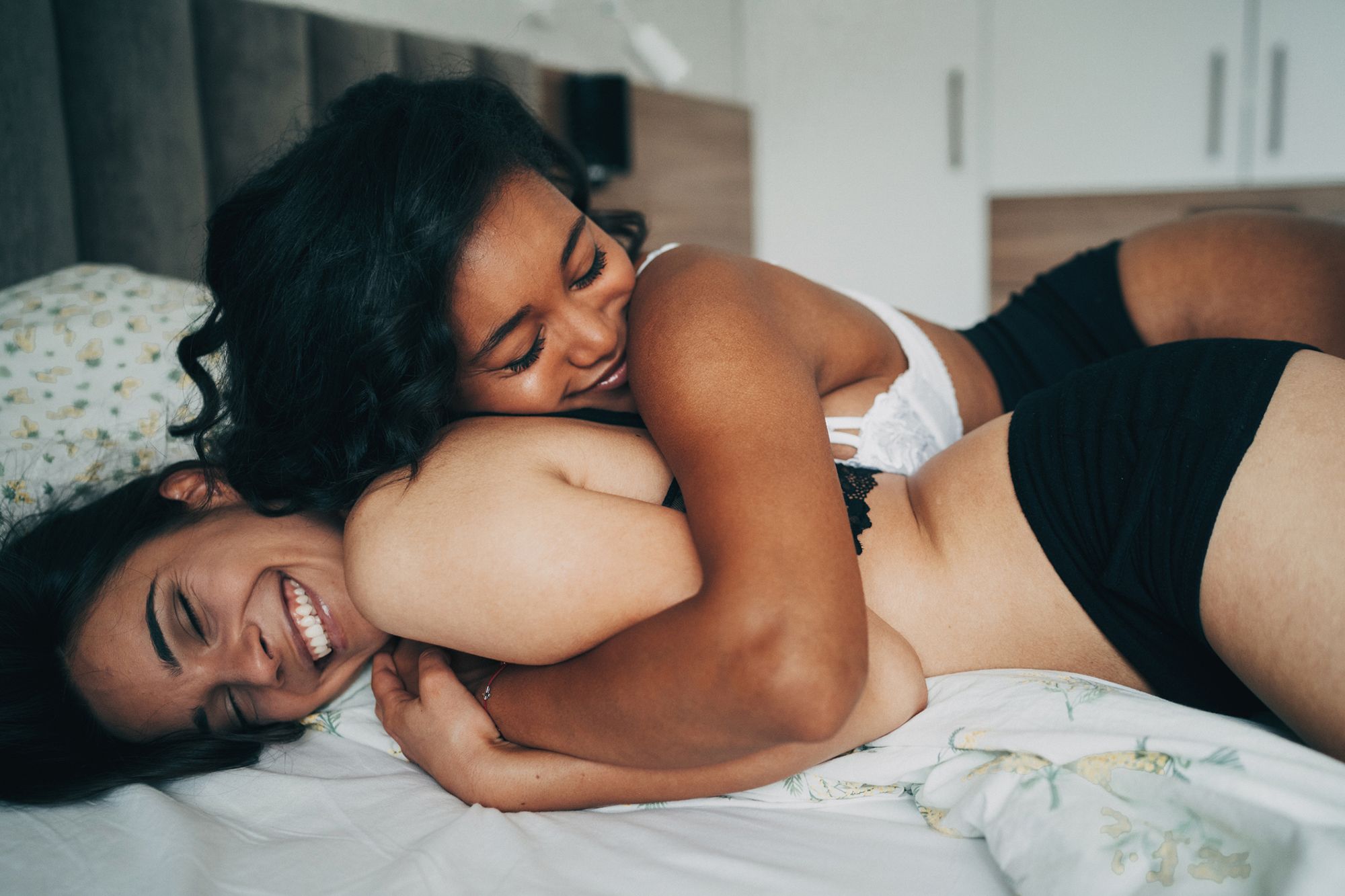 2 Frauen in Unterwäsche liegen im Bett und umarmen sich