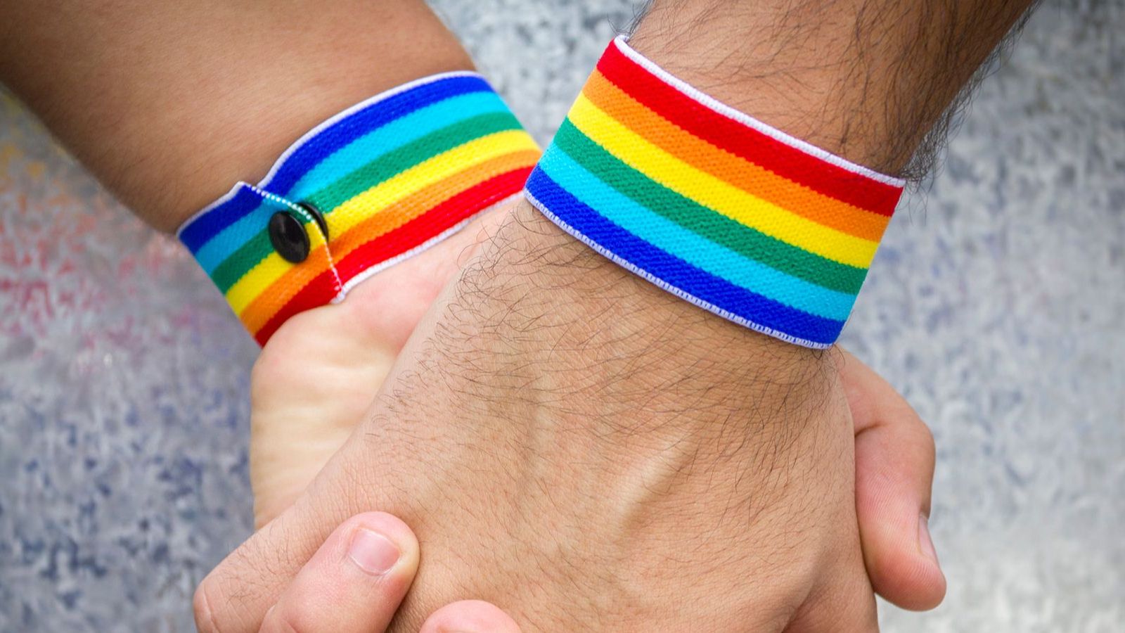 Zwei ineinander verschränkte Hände mit Regenbogen-Armbändern