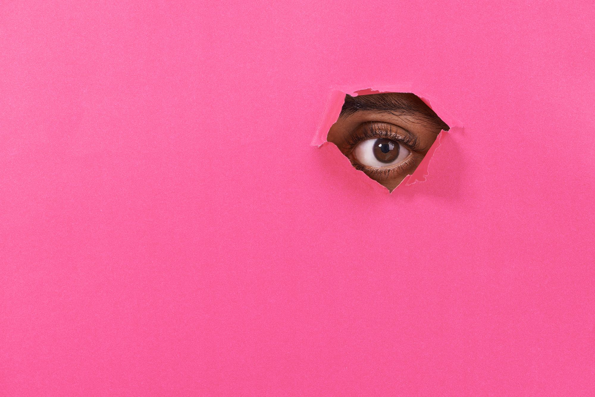 Auge, das durch ein Loch in einem rosa Plakat schaut