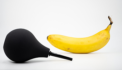 Eine schwarze Analdusche und eine Banane vor einem weißen Hintegrund