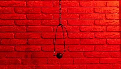 Ein schwarzer Mundknebel, der an einer Kette hängt, vor einer roten Backstein-Wand