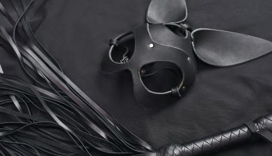 BDSM Zubehör: Eine schwarze BDSM Maske und eine schwarze Peitsche auf einem schwarzen Hintergrund